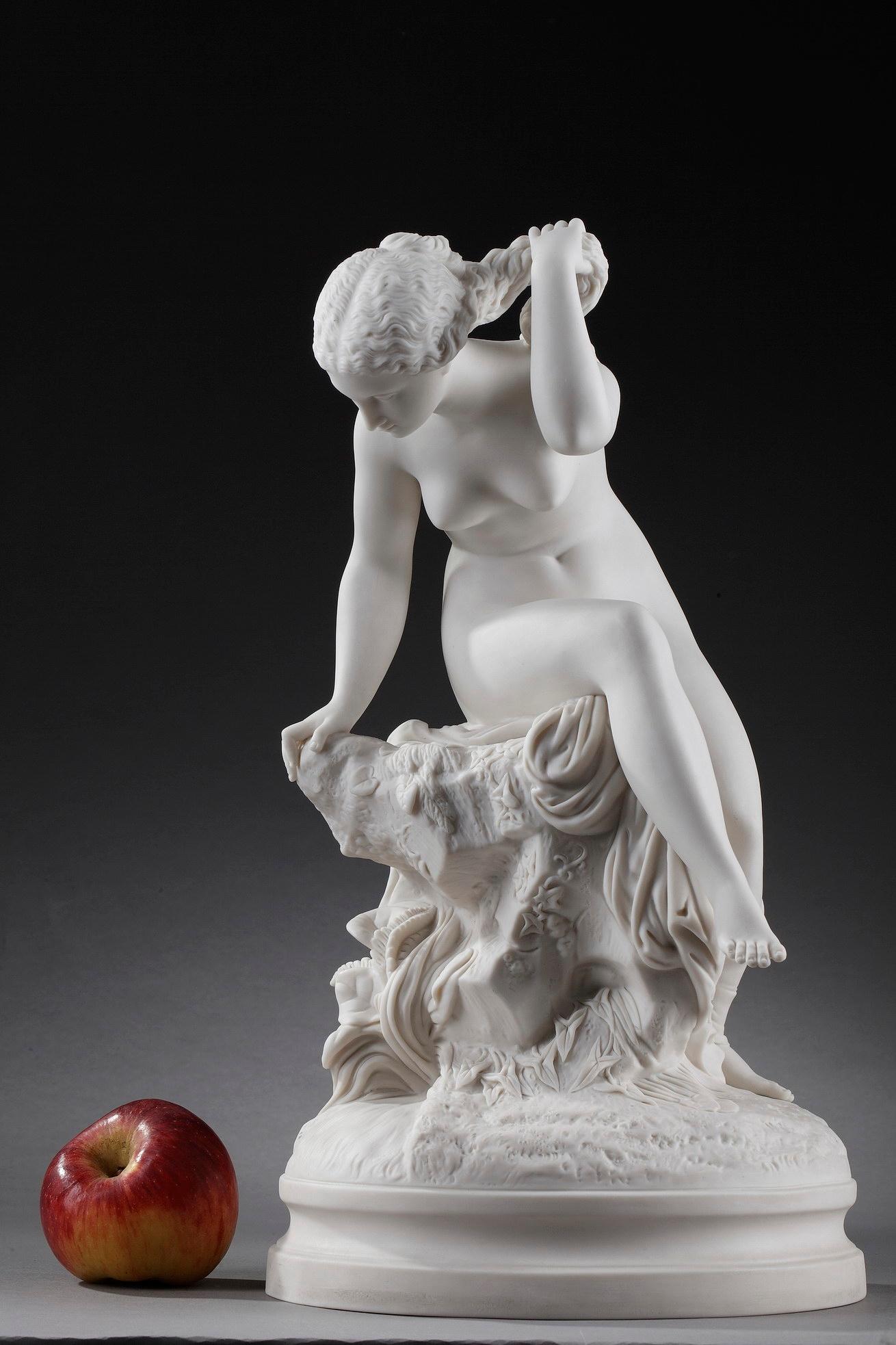 Art nouveau-period bisque porcelain figurine in the taste of Sevres, featuring a naked bather sitting on a rock, richly covered with plants. She seems to look at her reflection in the water while gracefully raising her hair on her neck. Perfectly