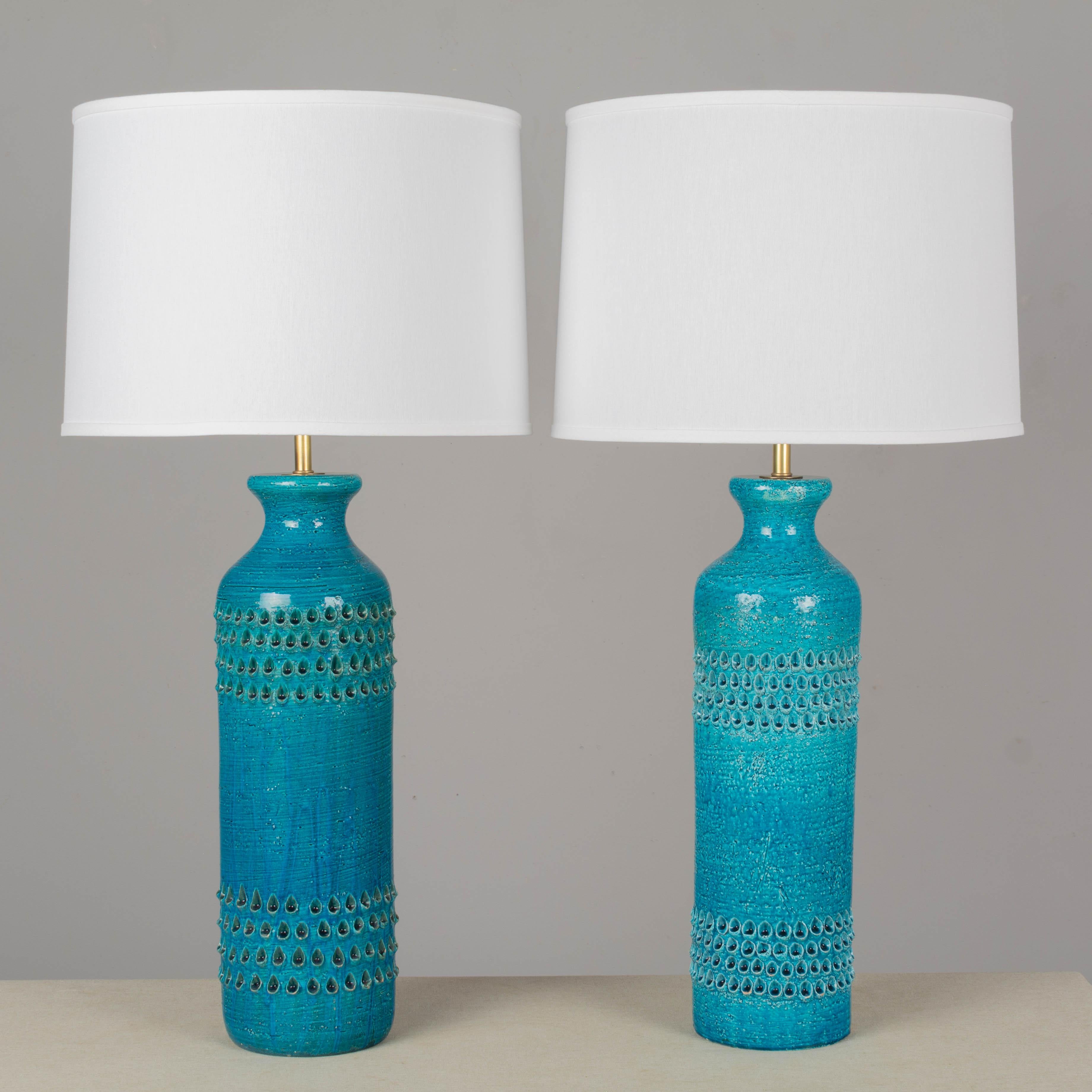 A pair of Bitossi ceramic table lamps by Aldo Londi with deep turquoise Rimini blue glaze. Large scale chunky pottery decorated in Lacrima pattern of impressed textured teardrops. Minor loss to some of the relief, one lamp with chip to bottom edge.