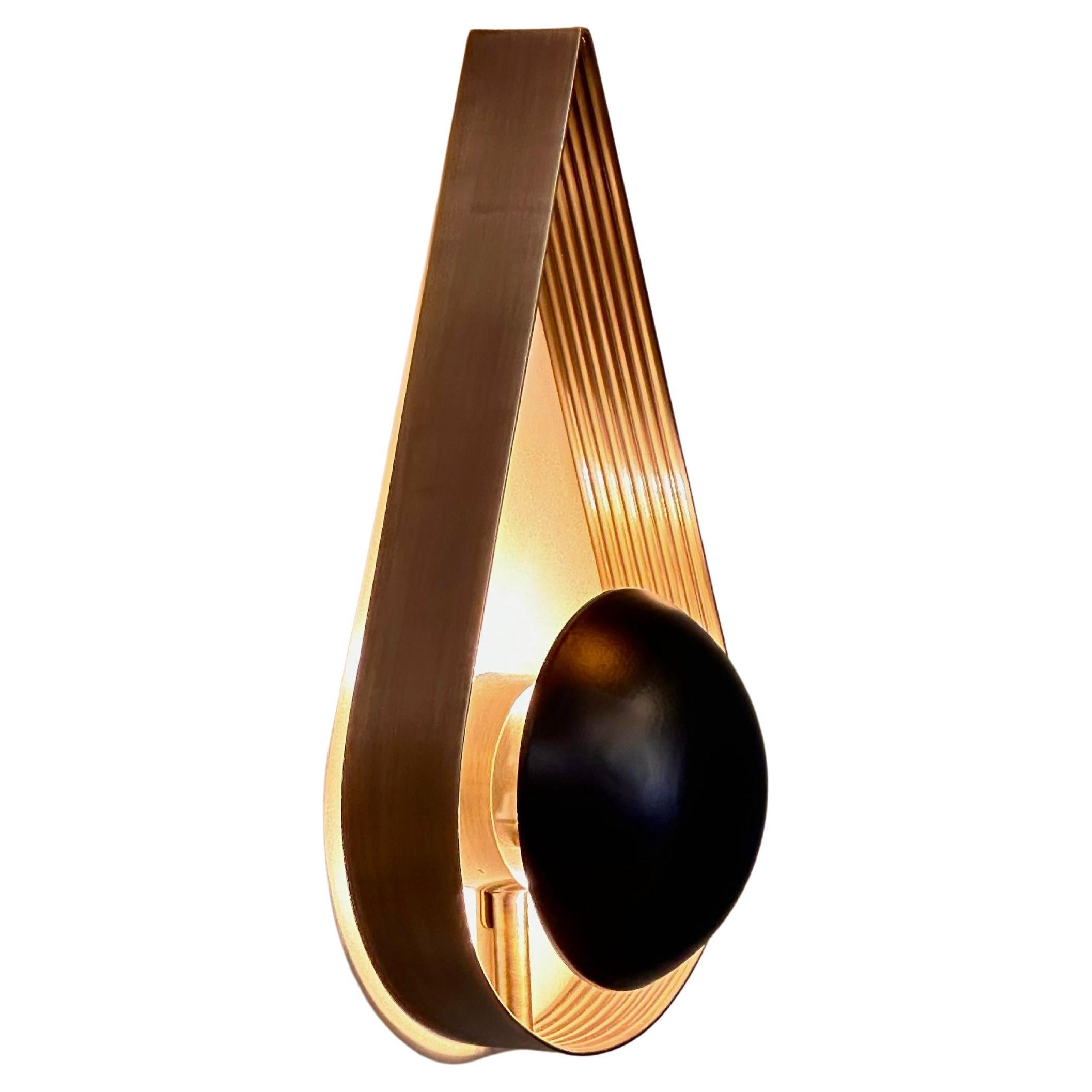 L'applique in ottone BITOLA è un apparecchio d'illuminazione moderno di metà secolo che unisce senza sforzo un'eleganza senza tempo a una funzionalità moderna. Realizzata con una lastra di ottone a righe posizionata verticalmente, l'applique assume