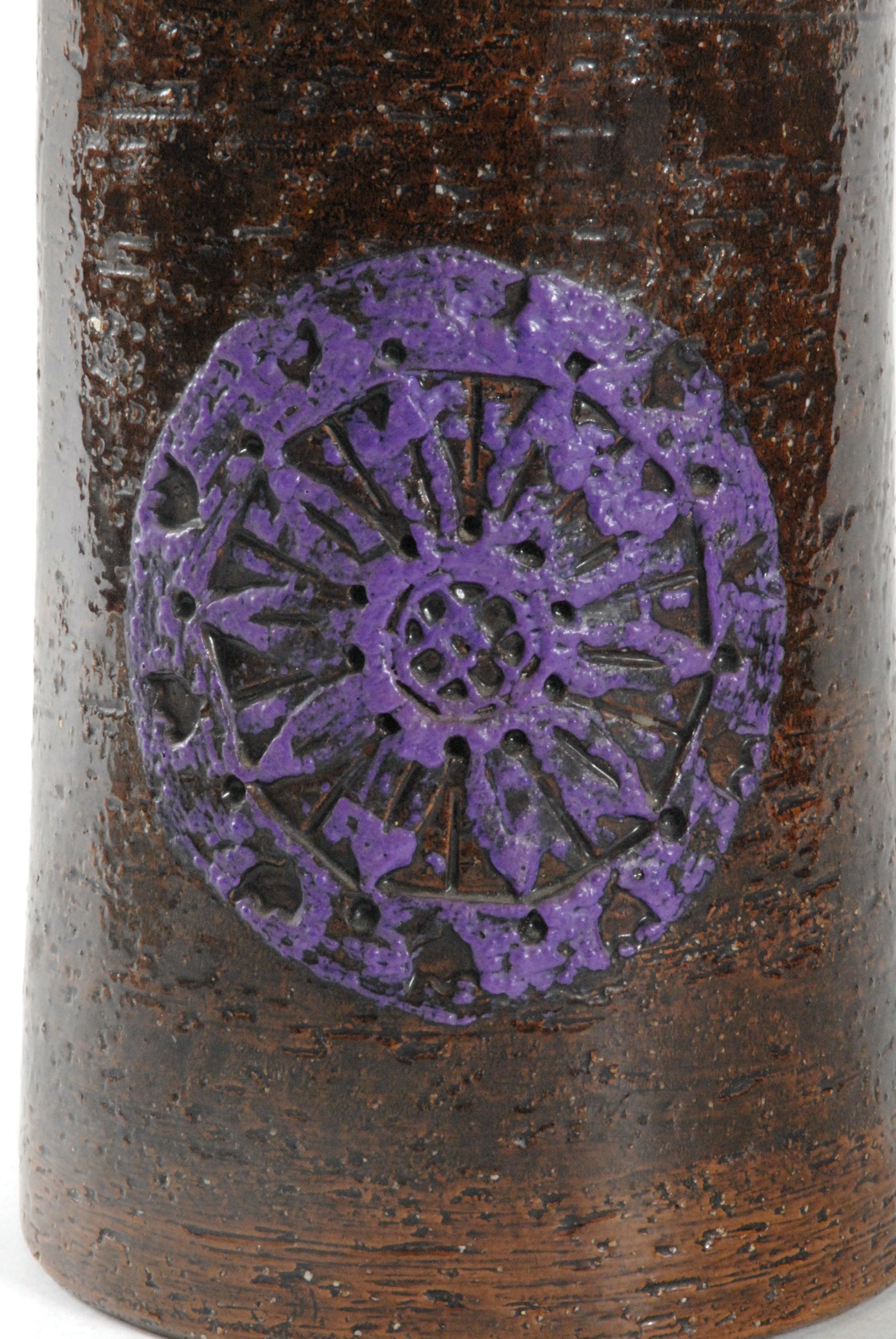 A large cylindrical vase with shaped top and the brown manganese body is decorated with purple acid resist circular motifs. Designed by Aldo Londi for Bitossi.