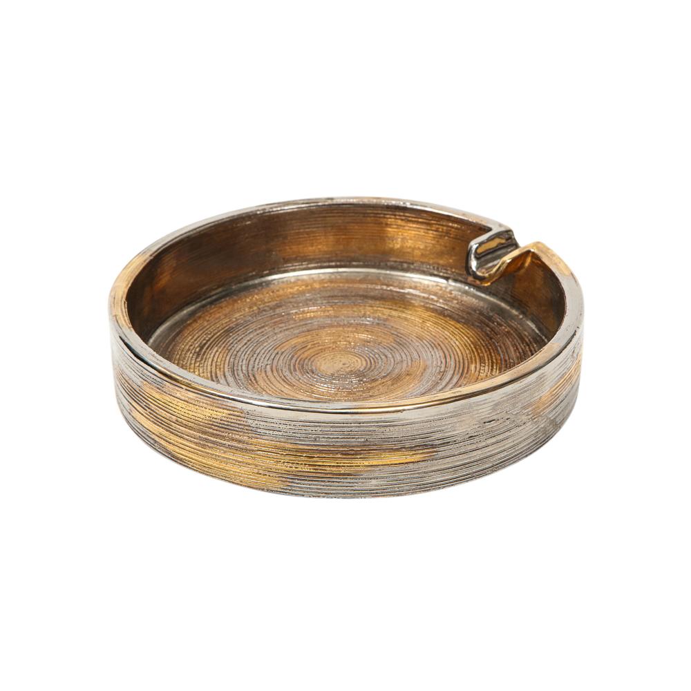 Bitossi ashtray, brushed metallic gold, chrome silver, signed. Small scale circular ashtray with a footed base and a single cigarette rest, decorated with a pattern of concentric circles and glazed in brushed metallic gold and platinum. Retains