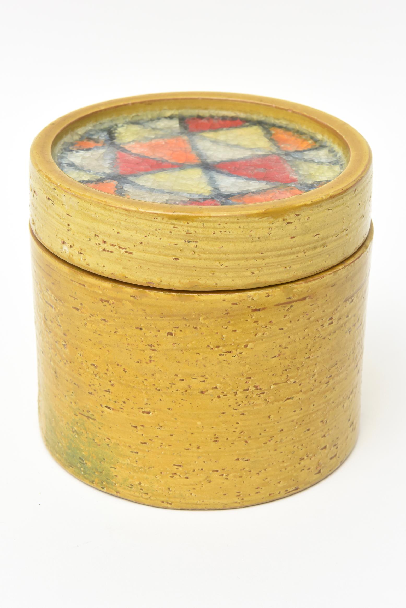 This lovely vintage Bitossi for Raymor glazed ceramic round lidded box is from the 1960s and is Italian. It has the fused glass mosaic insert on the top. The rich color of the mustard yellow exterior plays well with the multicolored broken fused