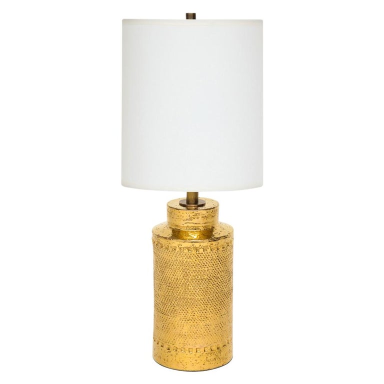 Bitossi lamps, gold ceramic, signed. Pair of cylindrical table lamps with stepped necks and stippled textured bodies. The Bitossi factory mixed 24-karat gold to achieve the luster to their gold glazes. Both lamps retain their original paper labels