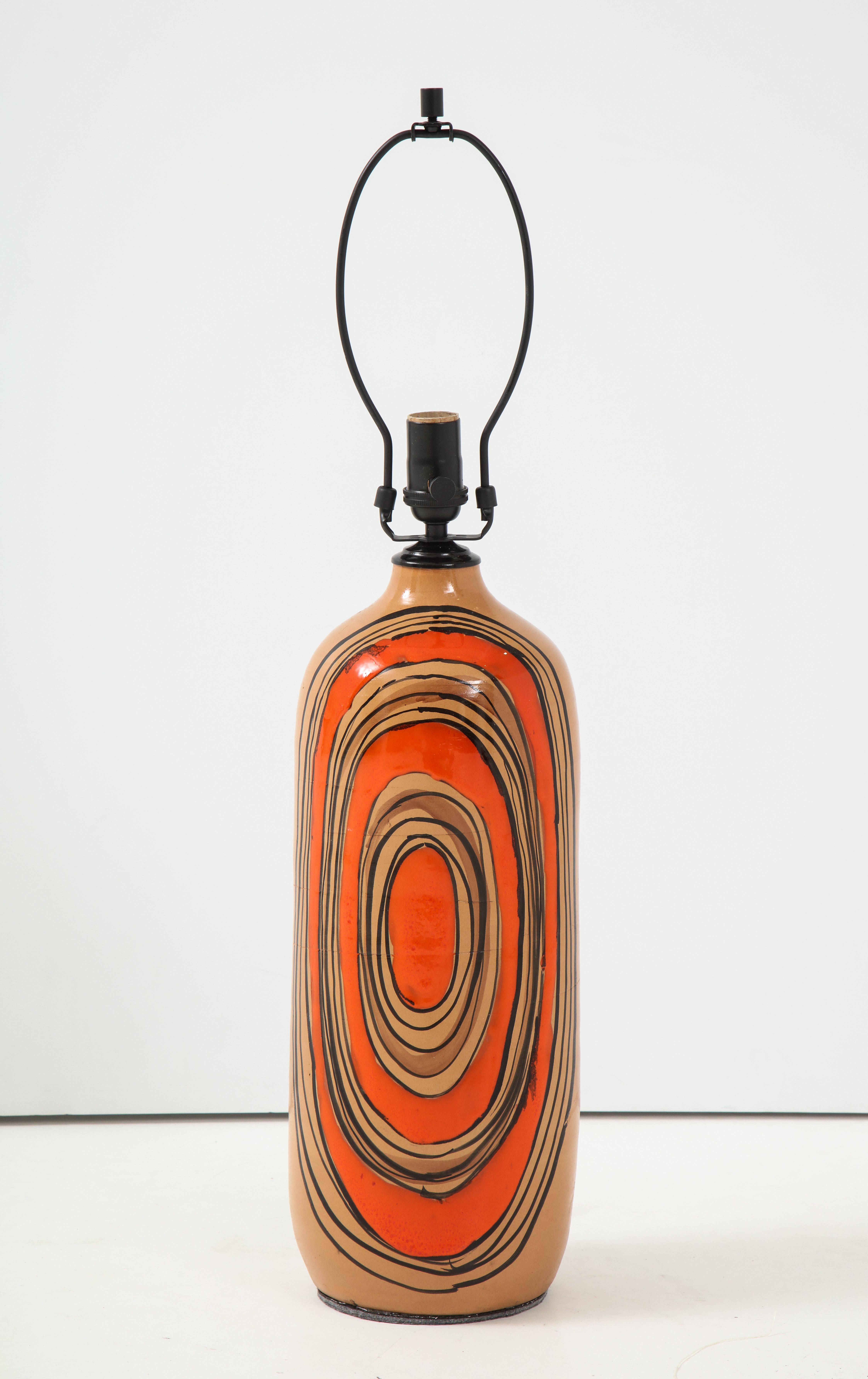 Pair of modern ceramic lamps with a sand colored glazed bodies and contrasting orange and black exuberant ovals, Signed on bottom. Rewired, 100W max bulbs.