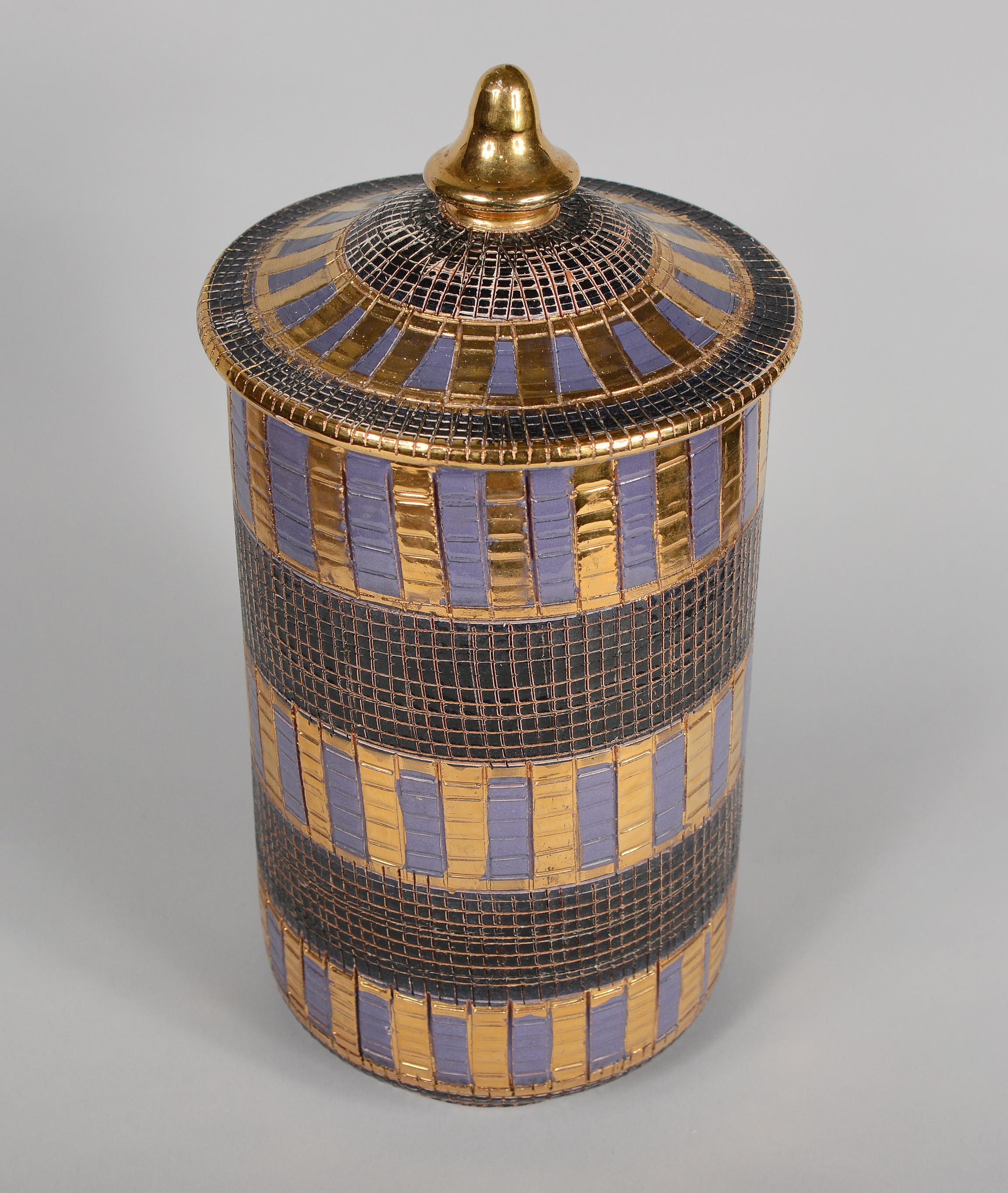 Covered jar from the Seta Series by Bitossi. This has gold and purple glaze with gold highlights. There are two small chips on the edge of the lid. There are few tiny glaze flakes on the edge of the jar rim.