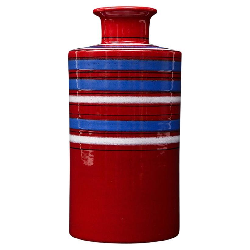 Vase Bitossi Raymor, céramique, rouge, bleu, blanc, rayures, signé. Vase cylindrique de petite taille à la forme moderniste et décoré de rayures rouges, bleues et blanches. Lèvre évasée. Le col mesure 1,32 pouces. L'étiquette en papier de Raymor