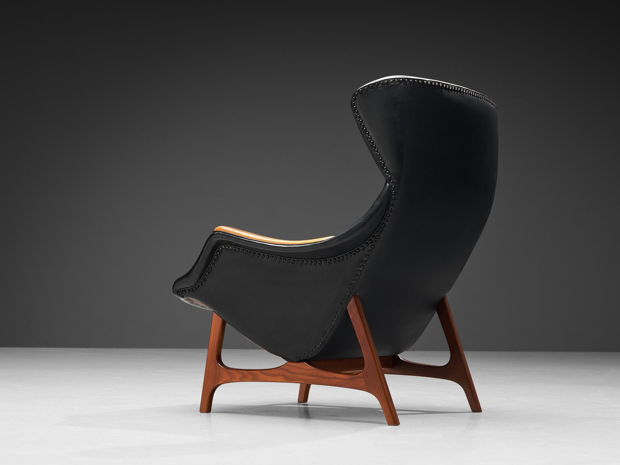 BJ. Hansen, lounge chair, leatherette, teak, metal, Norway, produced in Sjøholt, 1960s. 

This high-quality wingback chair is based on a solid construction featuring round and bold shapes. The seating is designed as a shell that embraces the sitter