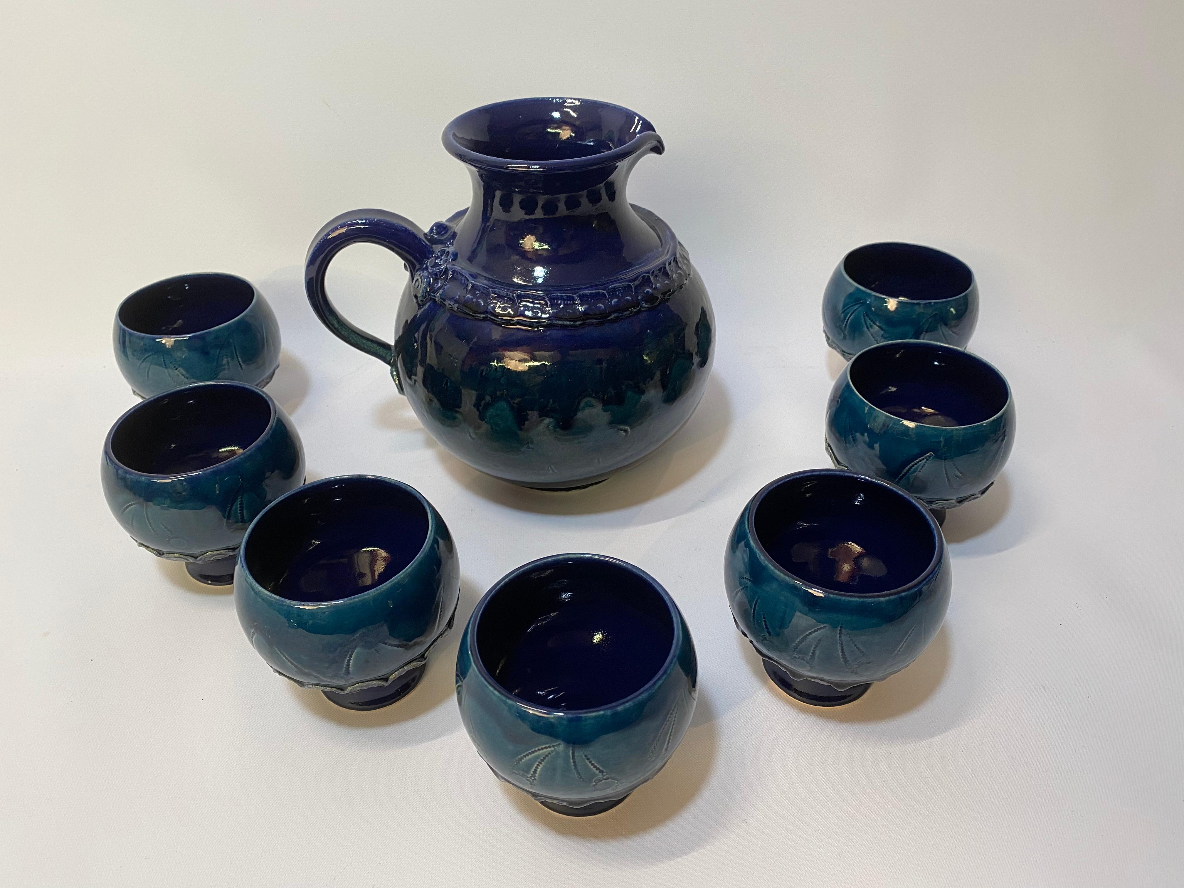 Bjorn Wiinblad for Rosenthal ceramic pitcher and cups. One large pitcher with seven cups. Glossy two-tone blue glaze. Impressed floral design Good overall condition with some tight crazing to the glaze. No visible chips, hairlines or restorations.
