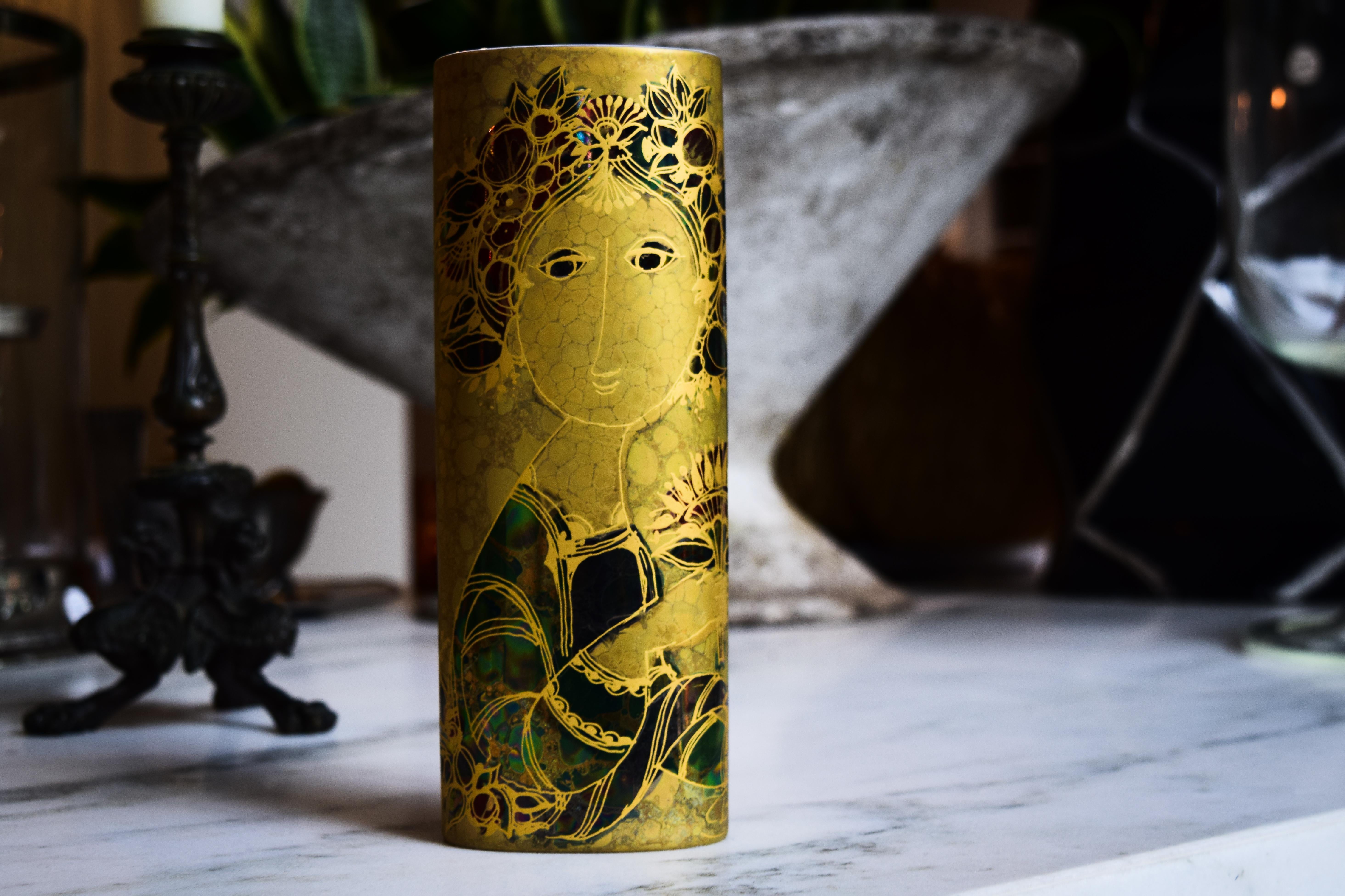 This vase is one example of the captivating style brought to life by the whimsical mind of artist Bjorn Wiinblad. Delightfully colored in metallics and 24-karat gold, the vases feature the trademark round faces and complex detail that made Wiinblad