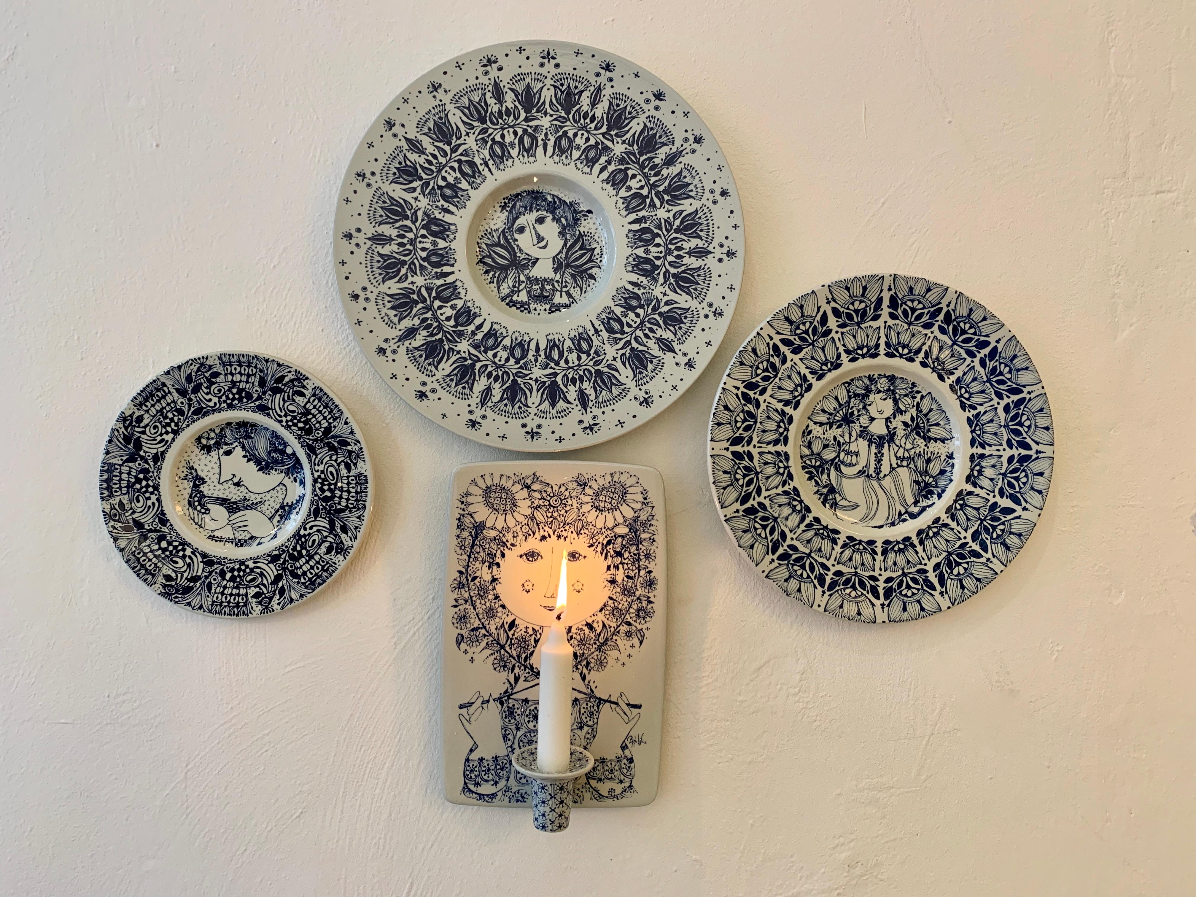 Bjørn Wiinblad (1918-2006) installation of 4 ceramic wall hangings, consisting of one candle holder wall plaque with one light arm + 3 different sized wall plates 
Made by Danish ceramist company Nymolle from the 1960's / early 70's. 

All pieces