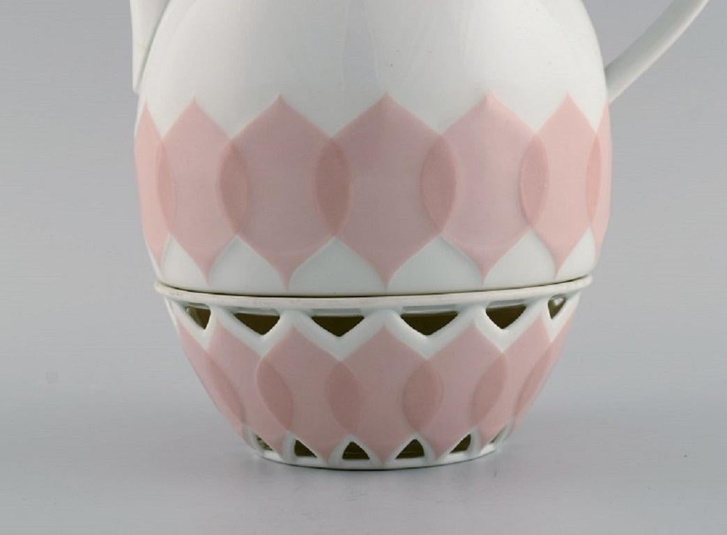 Bjørn Wiinblad für Rosenthal. Lotus-Porzellan-Service. 
Kaffeekanne mit Heizung für Teelichtkerzen, verziert mit rosa Lotusblättern. 1980s.
Maße: 22,5 x 22 cm (inkl. Heizung).
In ausgezeichnetem Zustand.
Gestempelt.