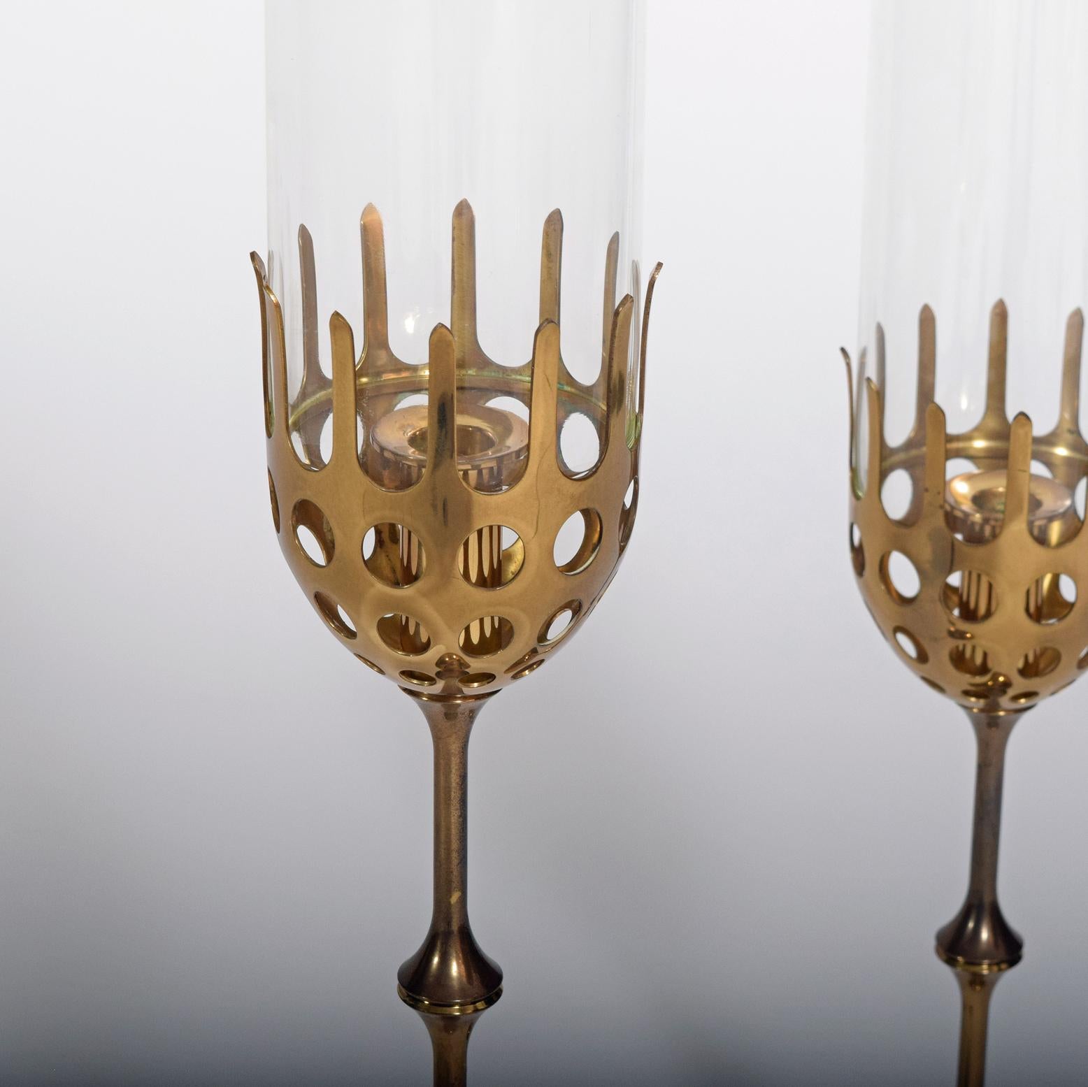 Bjørn Wiinblad: Two hurricane brass candlesticks with cylindrical clear glass shades. Marked monogram Bjørn Wiinblad, made in Denmark.
