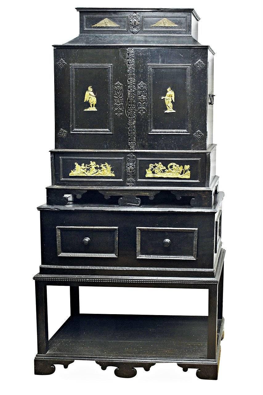 An 18th century Flemish ebonized and giltwood side cabinet with repoussé brass ornament,
The cabinet of stepped sectional form, the upper section with doors each with black painted repoussé rosette mounts and elaborately pierced escutcheon, with a