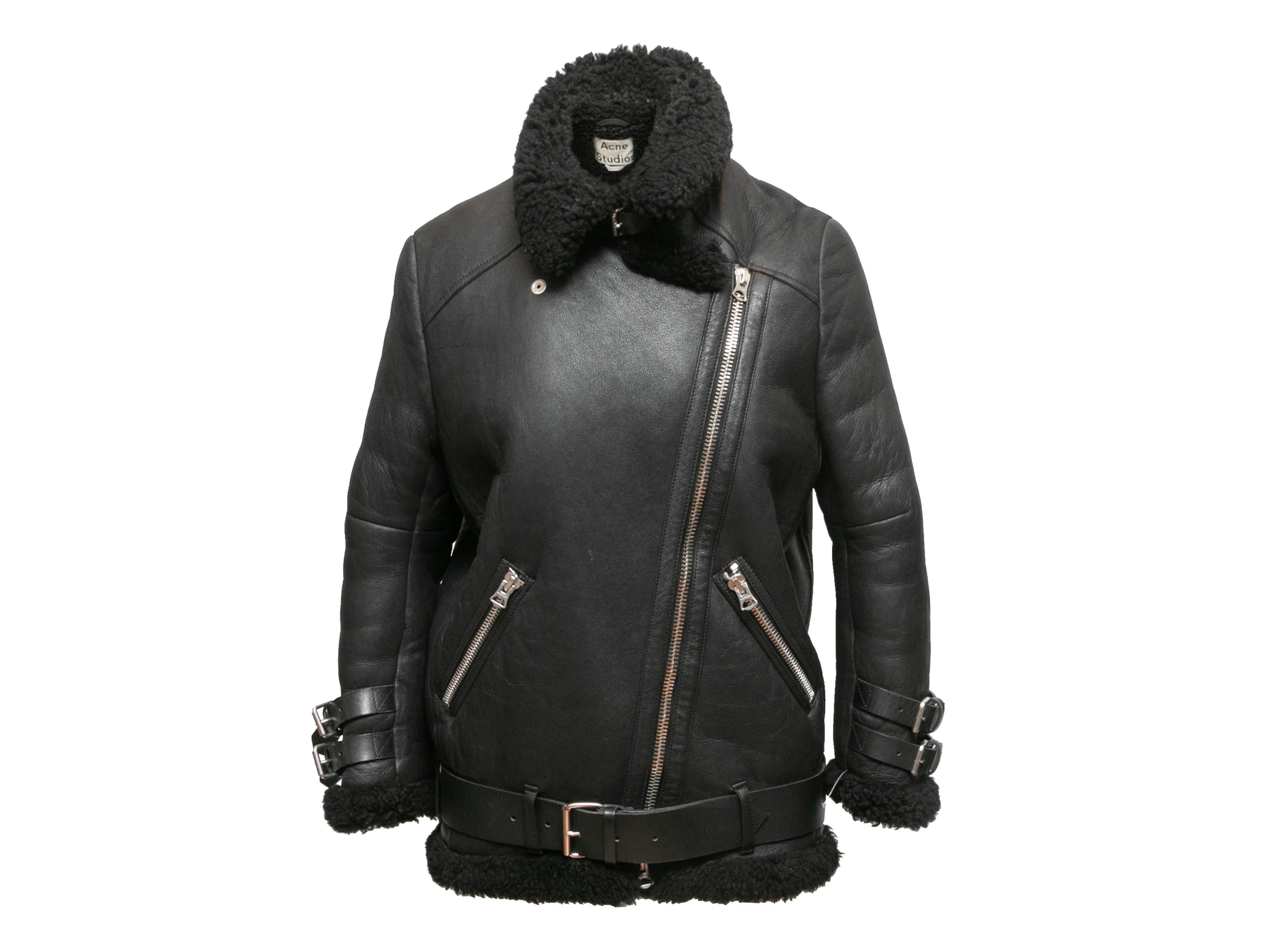 Black leather and shearling moto jacket by Acne Studios. Silver-tone hardware. Notched lapel. Buckle accents at cuffs. Dual zip closure hip pockets. Belt at waist. Zip closure at front. 32