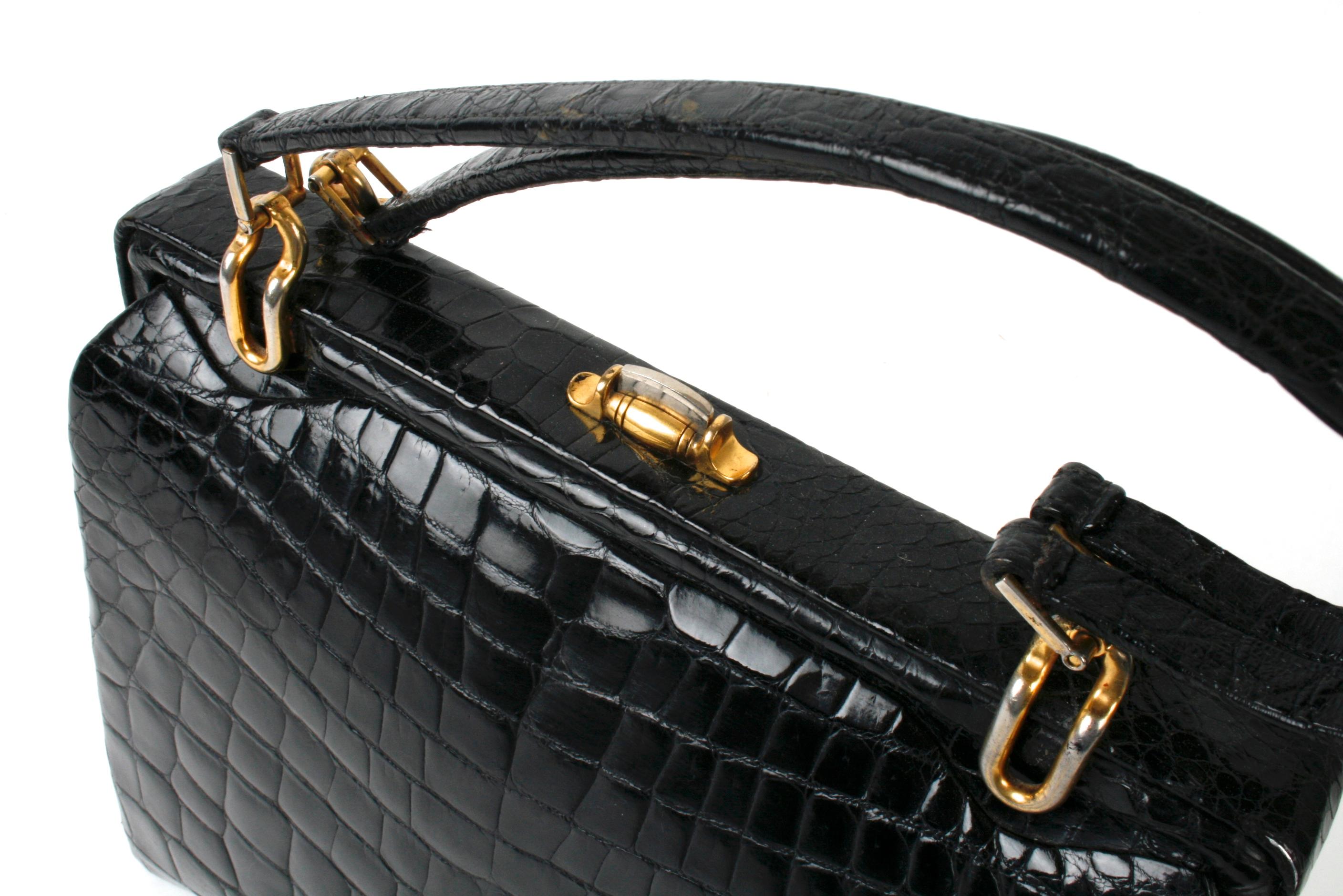 Black alligator handbag with matching double straps and gold-tone link hardware. It has double accordion construction,  a two-tone push-button closure and a wide hinged opening. The purse is lined in a soft tan suede with two alligator lined side