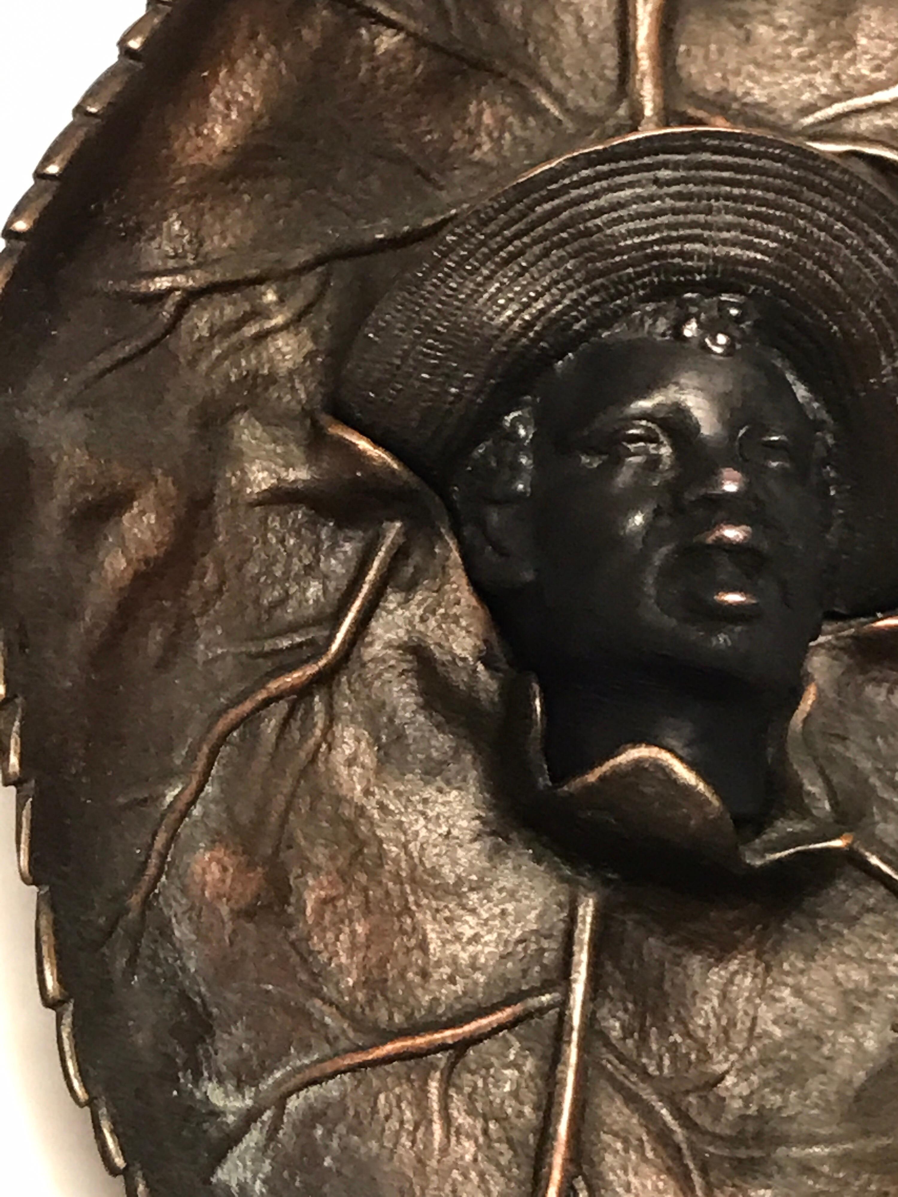 Black Americana boy with straw hat tobacco leaf plaque, realistically cast with the boy in the straw hat breaking through a tobacco leaf.