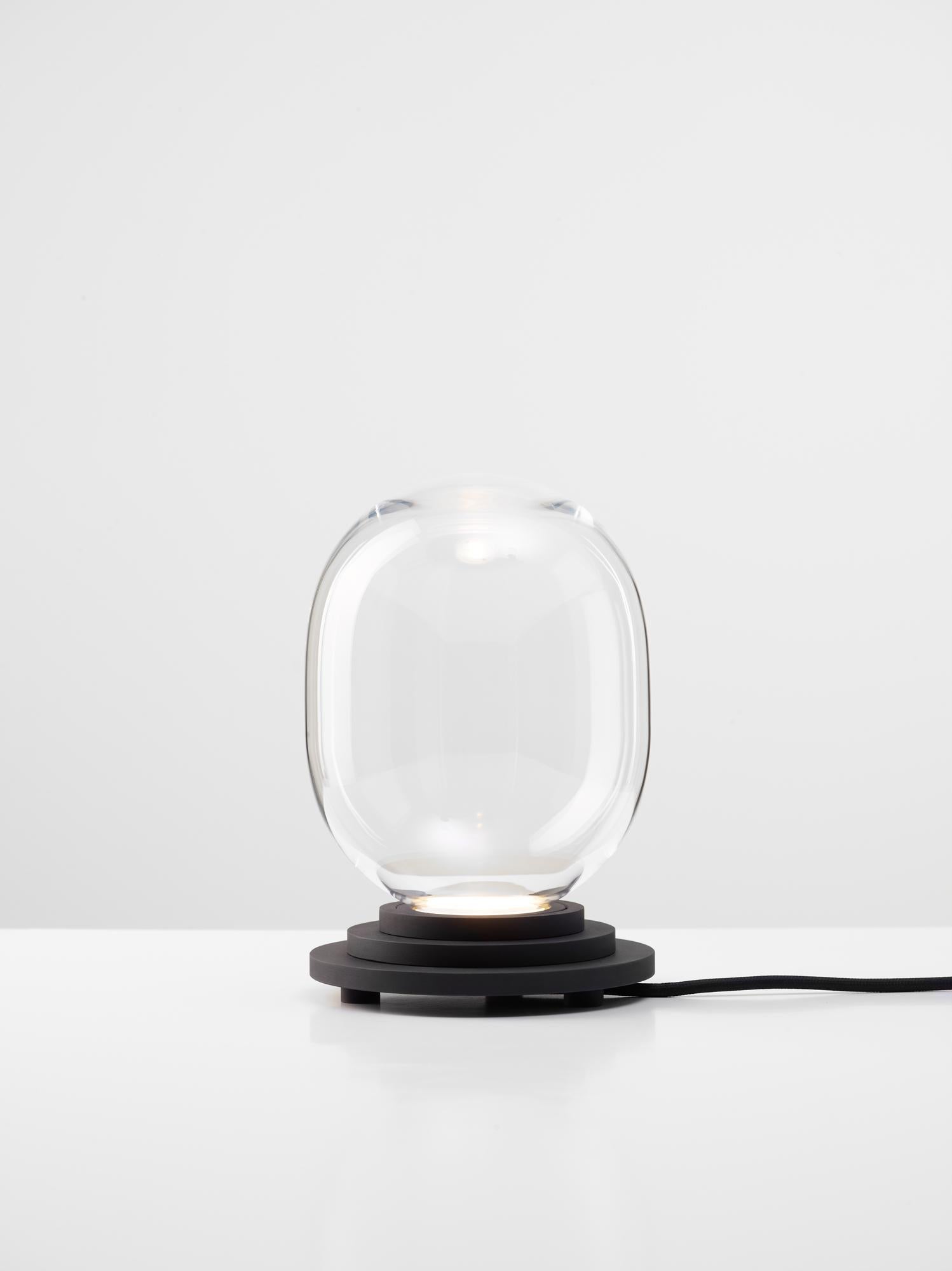 Black and clear Stratos Capsule table light by Dechem Studio
Dimensions: D 15 x H 22 cm
Materials: Aluminum, Glass.
Also available: Different colours available,

Different shapes of capsules and spheres contrast with anodized alloy fixtures,