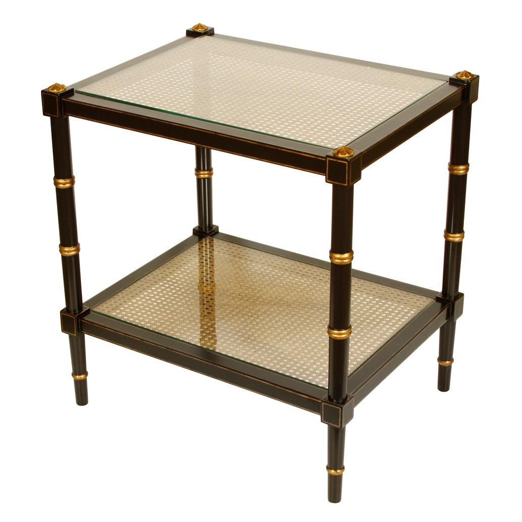A handsome two-tiered able in black with gold accents featuring two caned glass shelves. One of two in our inventory.