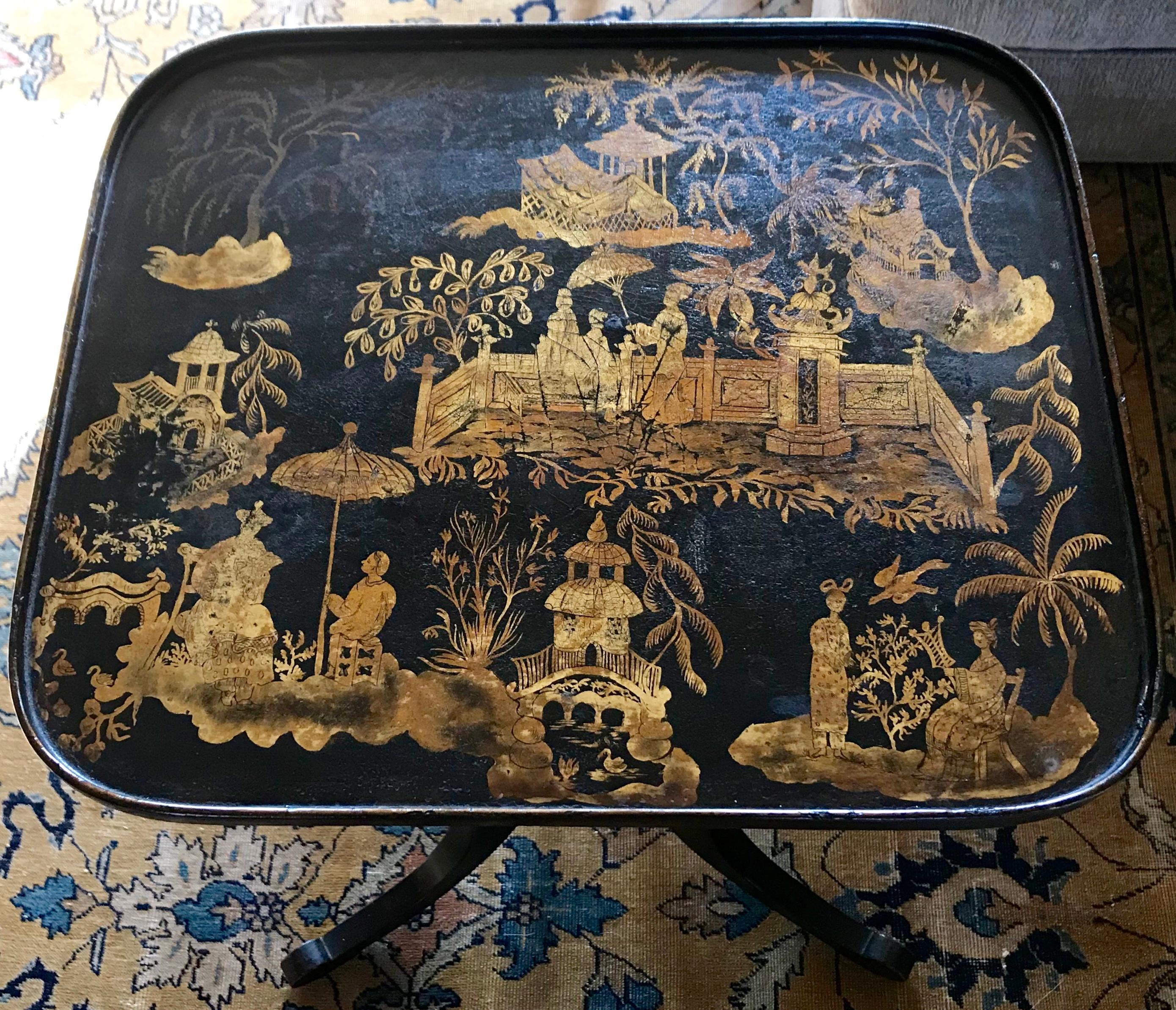 Black and gilt chinoiserie japanned side table. English japanned tripod candle-stand side table with shallow rim centering soft and varied gilt decoration of chinoiserie figures and pagodas in landscapes, on further decorated turned baluster base
