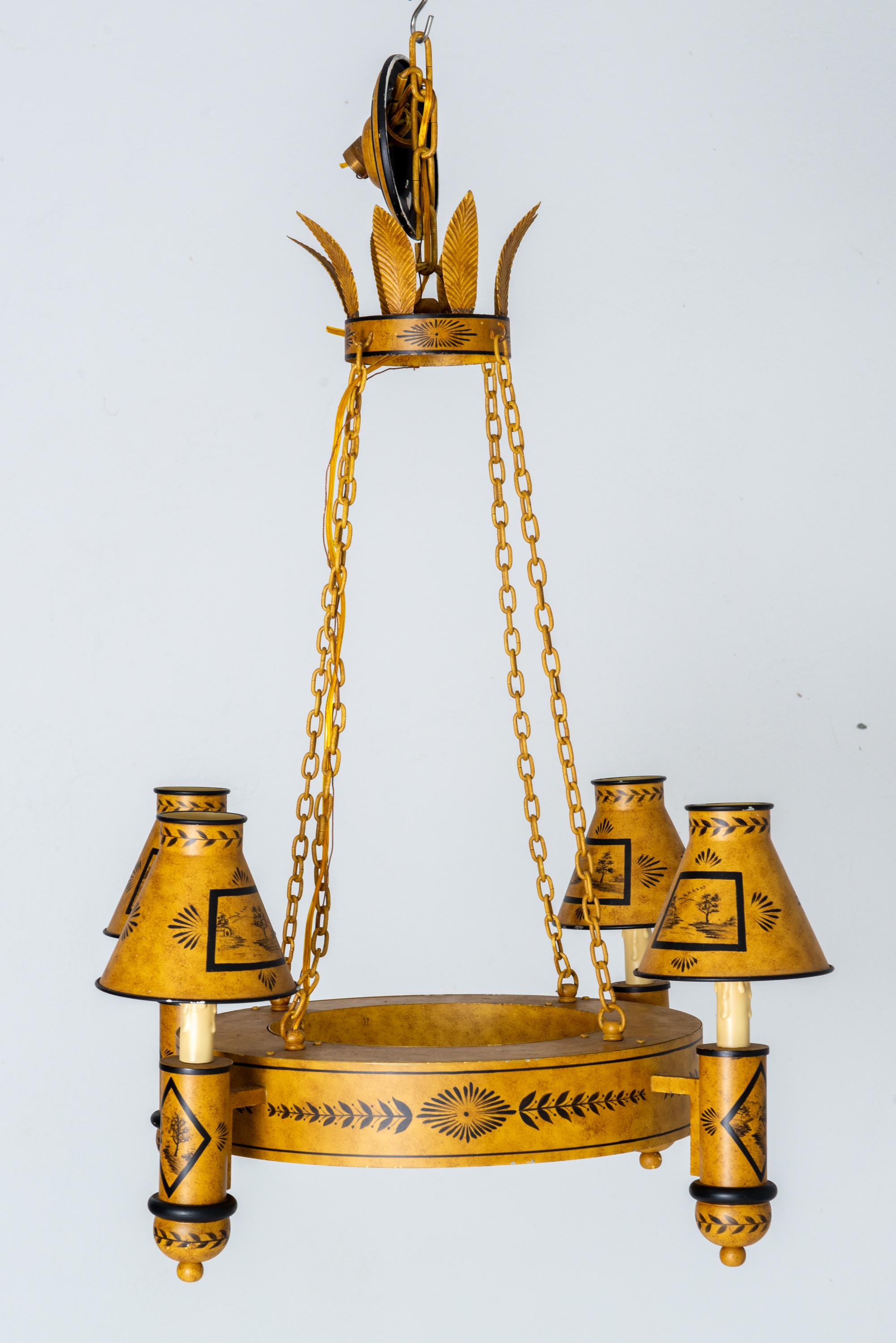 Un sorprendente lampadario vintage a quattro luci in tole dorate e nere, con paralumi in metallo svasati, risalente alla metà del XX secolo. L'apparecchio è dipinto a mano con delicate decorazioni in stile Impero o Direttorio. La corona di palme con