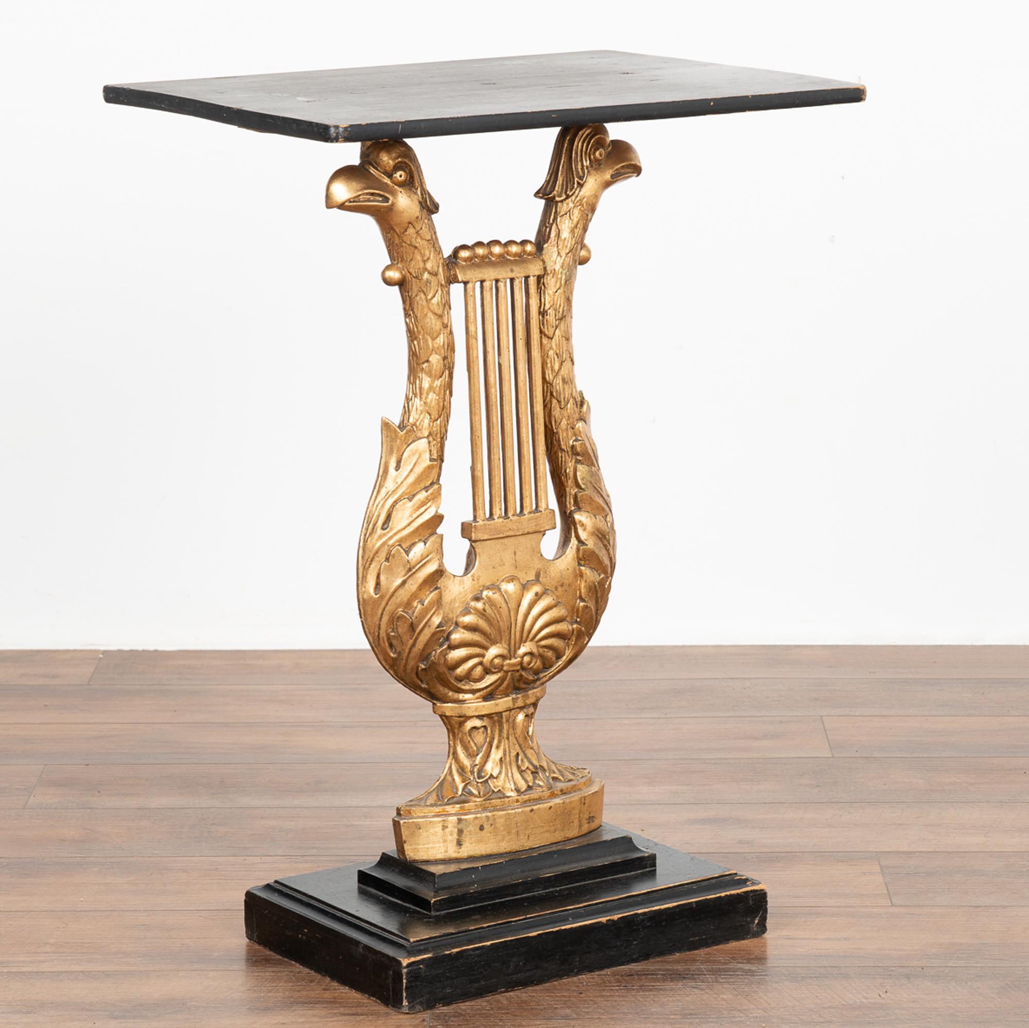 Des sculptures dramatiques de têtes d'aigle en forme de harpe forment la base de cette table console néoclassique de Suède.
La colonne centrale sculptée et peinte en or est complétée par le plateau et la base inférieure peints en noir.
Restauré,