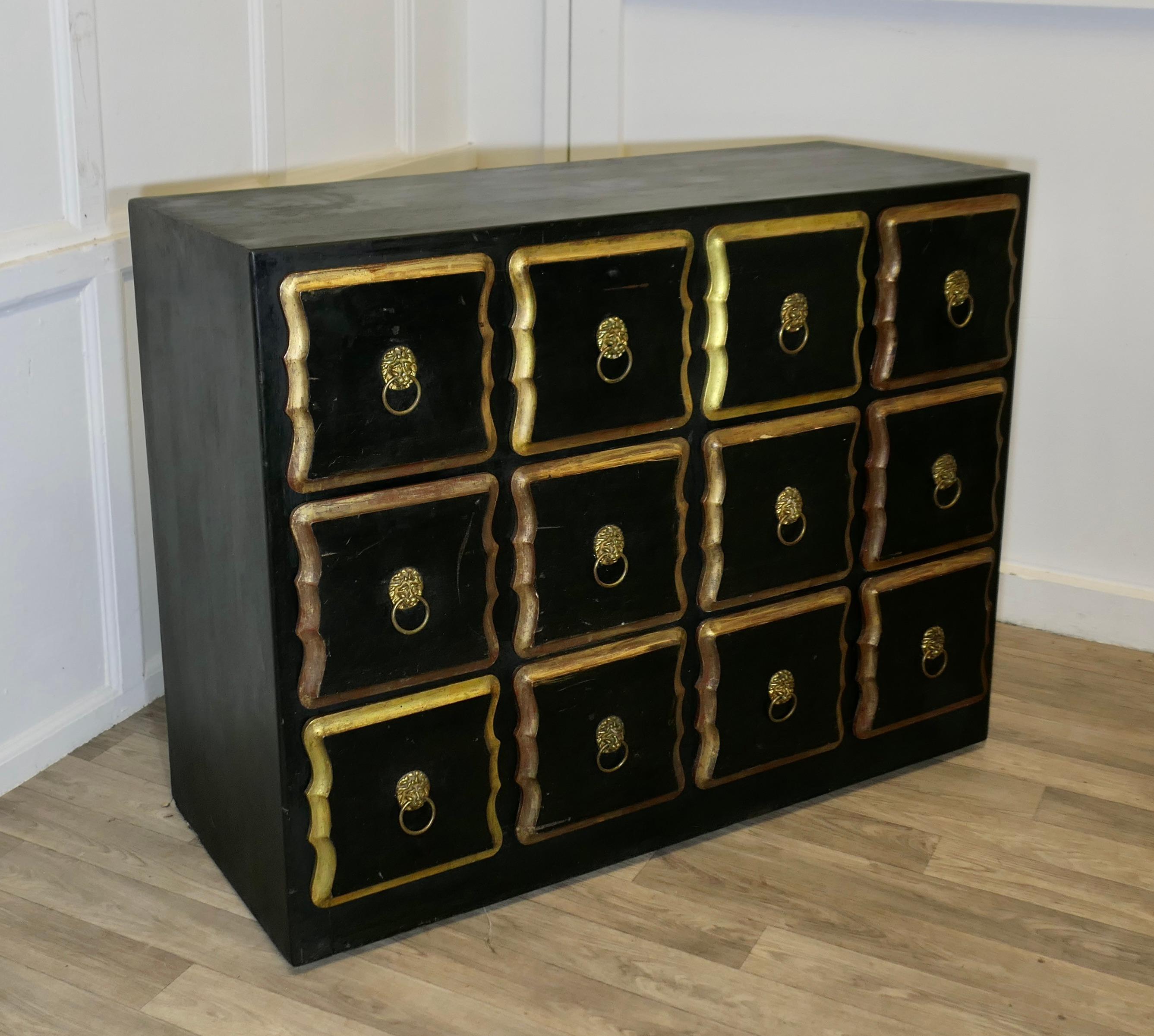 Armadietto del negozio Draper di merceria in oro e nero 

Si tratta di una grande cassettiera con un'insolita combinazione di 12 lunghi cassetti quadrati, con maniglie originali in ottone Lions Mask. 
La cassapanca è molto solida e pesante, in lacca