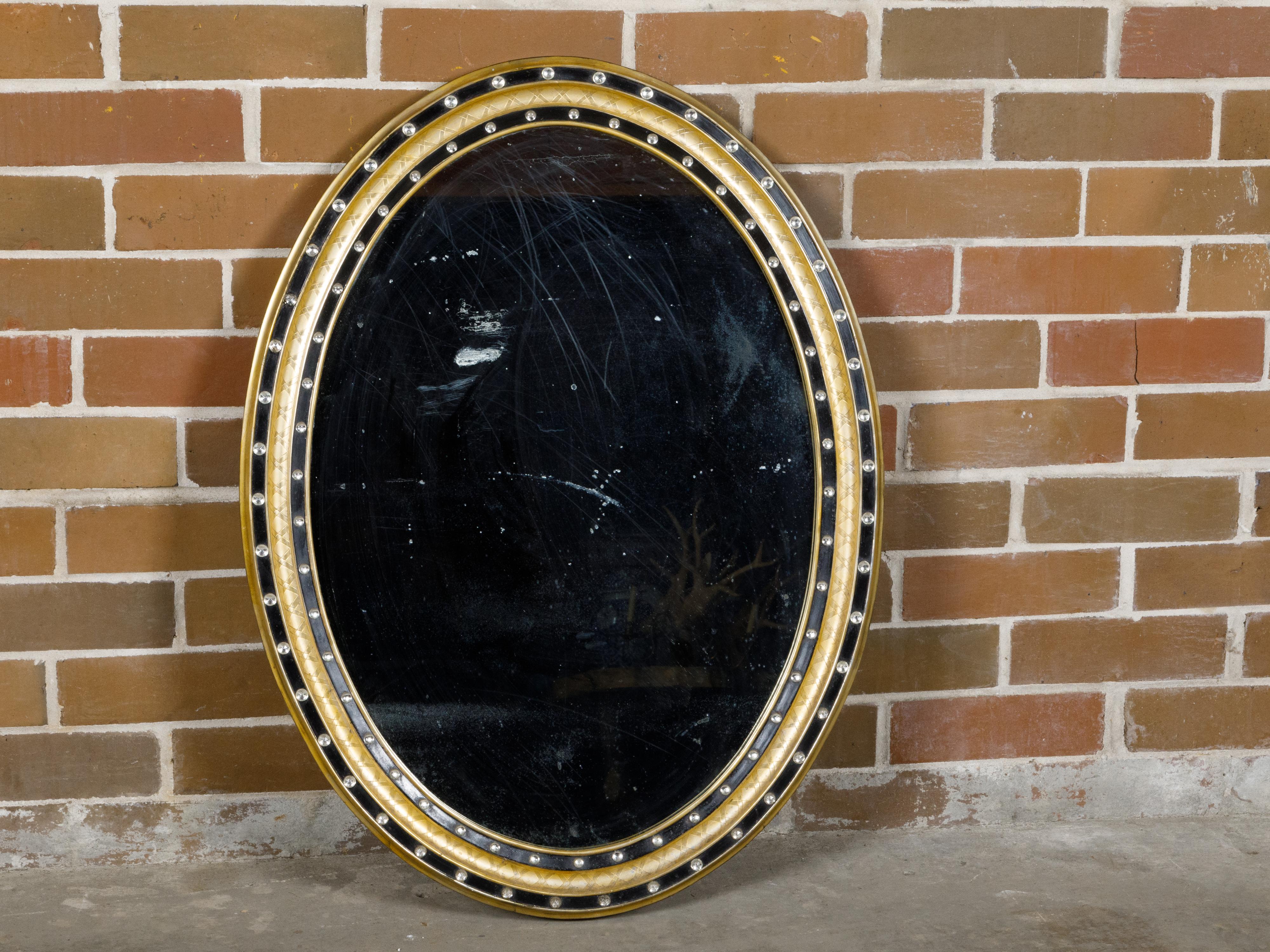 An Irish gilt and ebonized oval wall mirror from the 19th century with petite glass spheres and X-Form motifs. Immerse yourself in the elegance and charm of the 19th century with this Irish gilt and ebonized oval wall mirror. This exquisite piece,