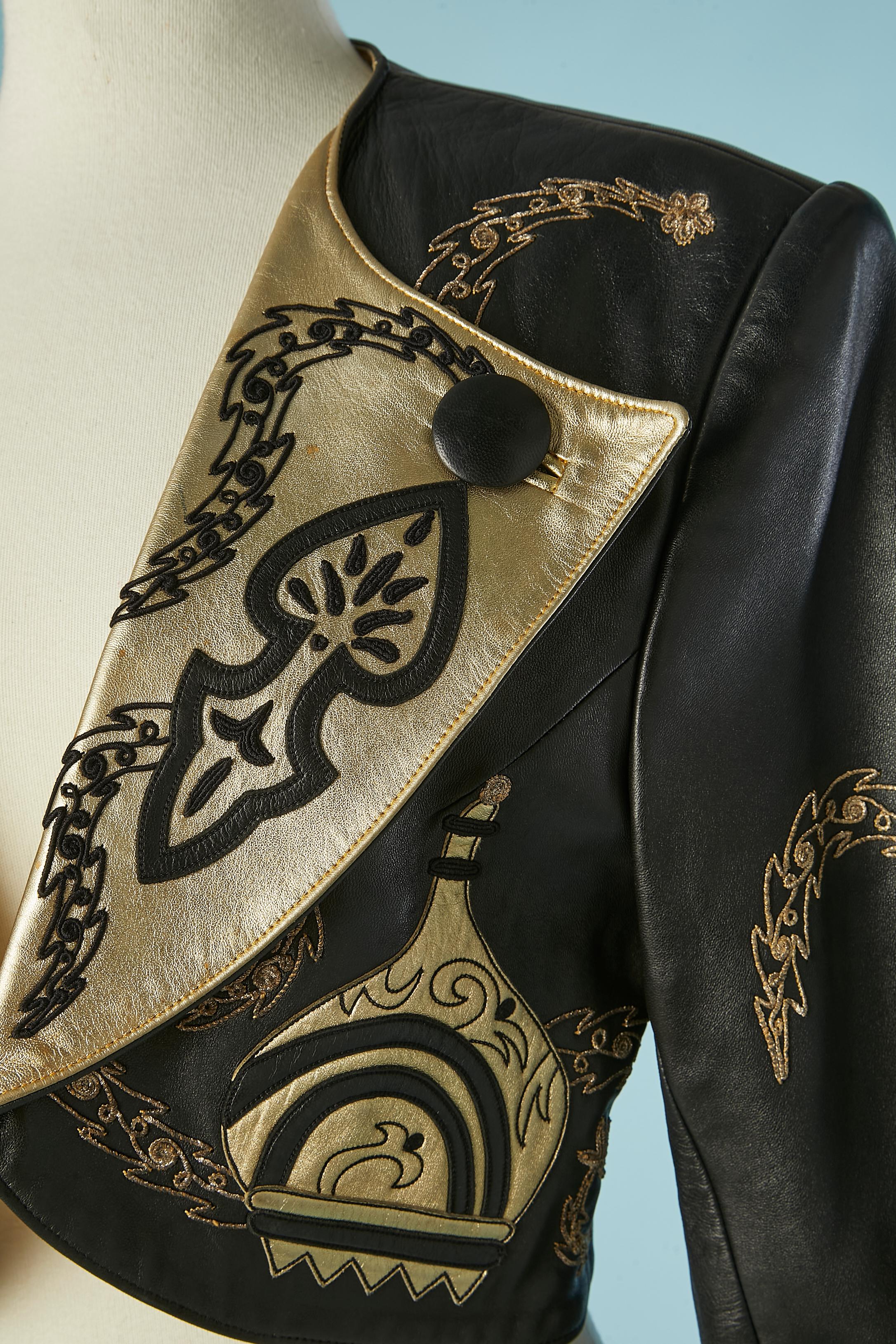 Boléro in pelle nera e oro. Fodera in acetato con marchio. 
Spallaccio. Bottone decorativo e asola sul colletto. Applicazioni in pelle nera e oro + ricami in filo di lurex 
TAGLIA M 