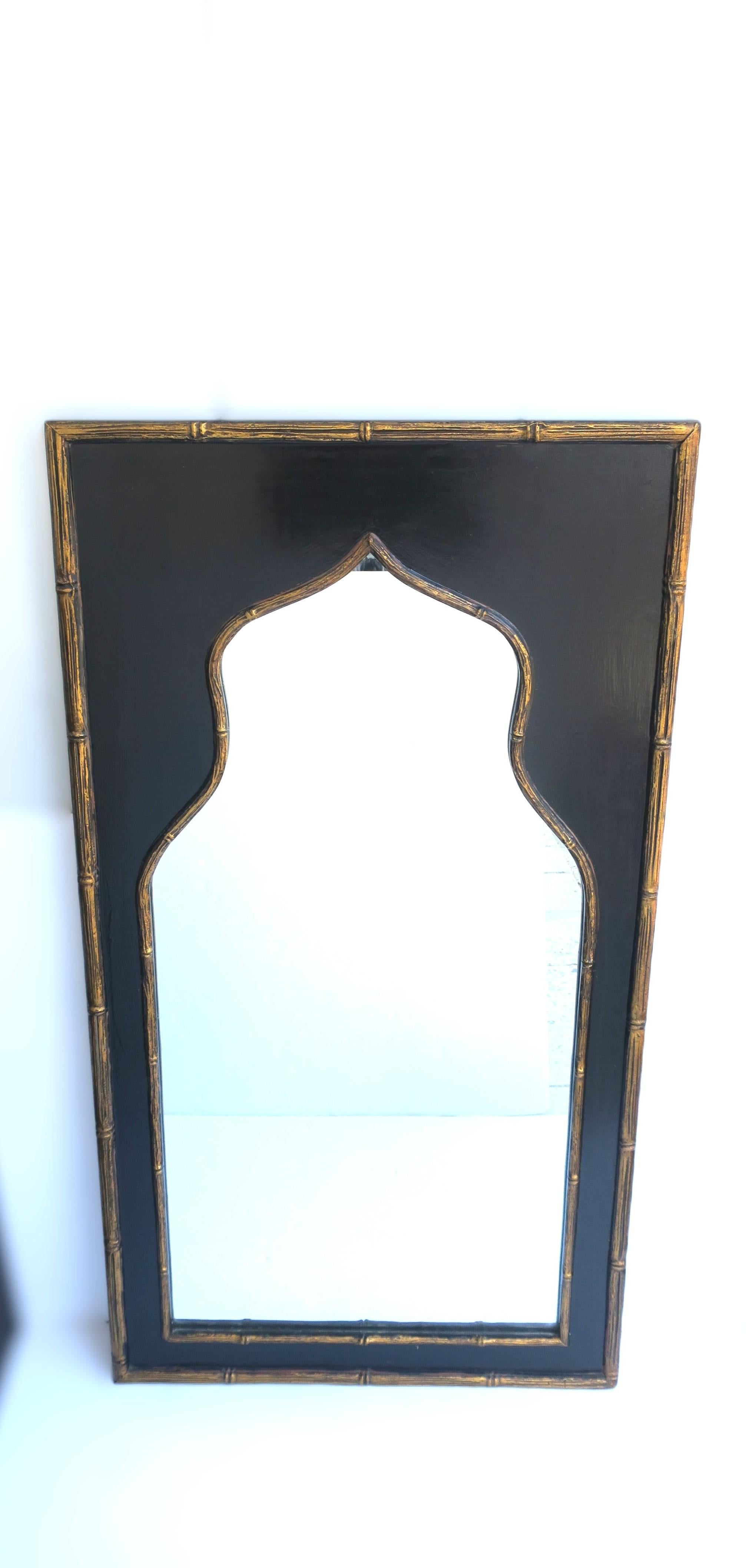 A beautiful black and gold gilt wall mirror with faux bamboo detail, in the Moorish design style, circa early mid-20th century, 1940s, USA. Mirror is rectangular with gold gilt faux-bamboo edge around black lacquer ground/in-between a gold gilt
