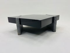 Tavolino geometrico nero e grigio, dal profilo basso e finitura lucida, con dettagli testurizzati