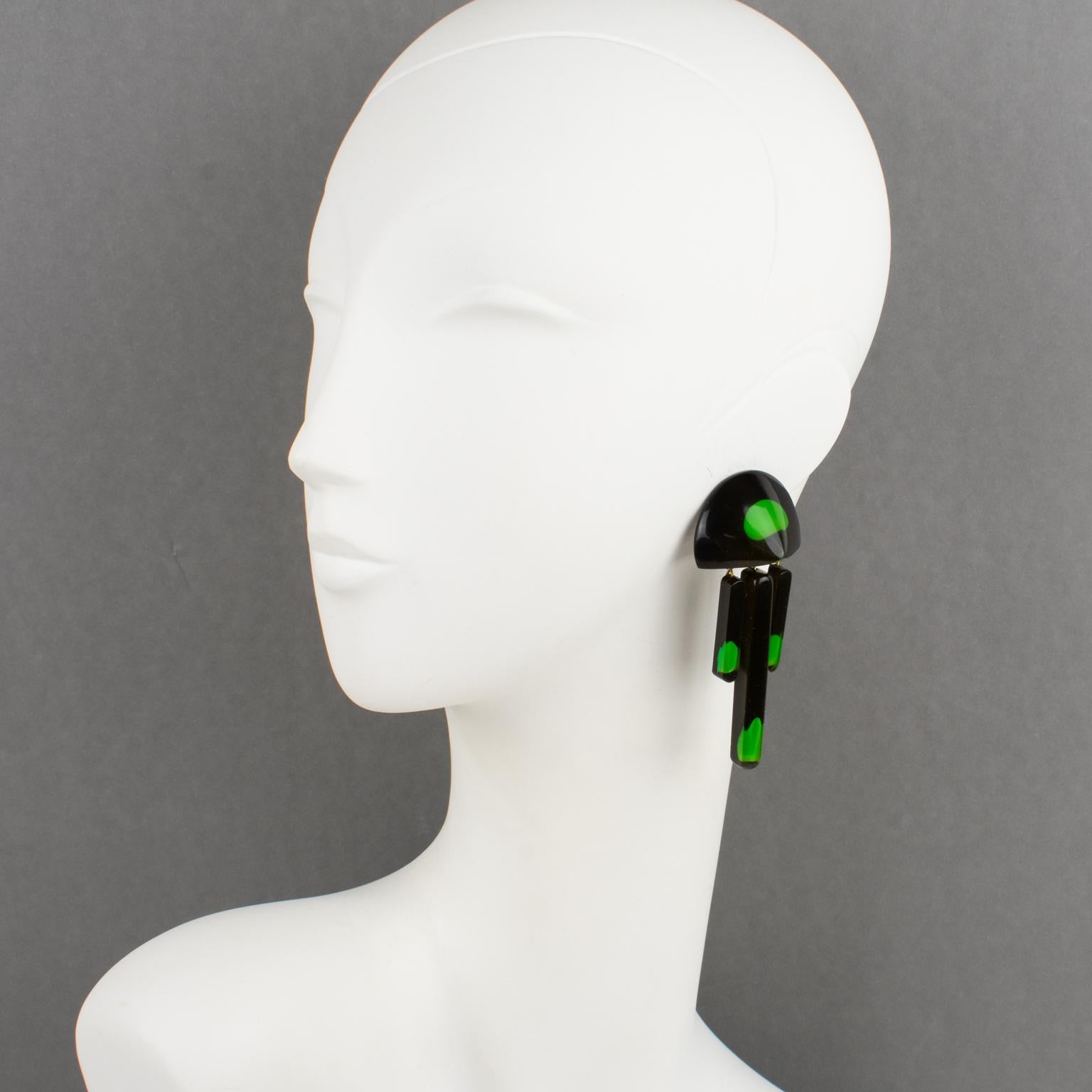 Ces étonnantes boucles d'oreilles clipsables modernistes en Lucite ou en résine acrylique présentent une forme géométrique dimensionnelle sculptée avec un fond noir surmonté d'inclusions de gouttes de gomme vertes noyées dans une couche de couleur