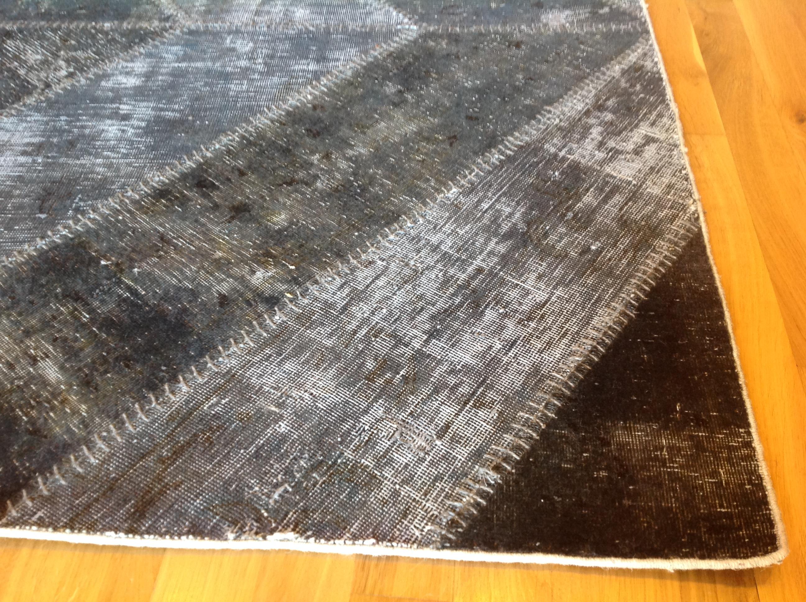 This highly unusual black and grey wool rug is a stunning example of the fruitful marriage of traditional design and modern overdying technique. Stitched borders add an extra element of visual interest. Made in Pakistan.