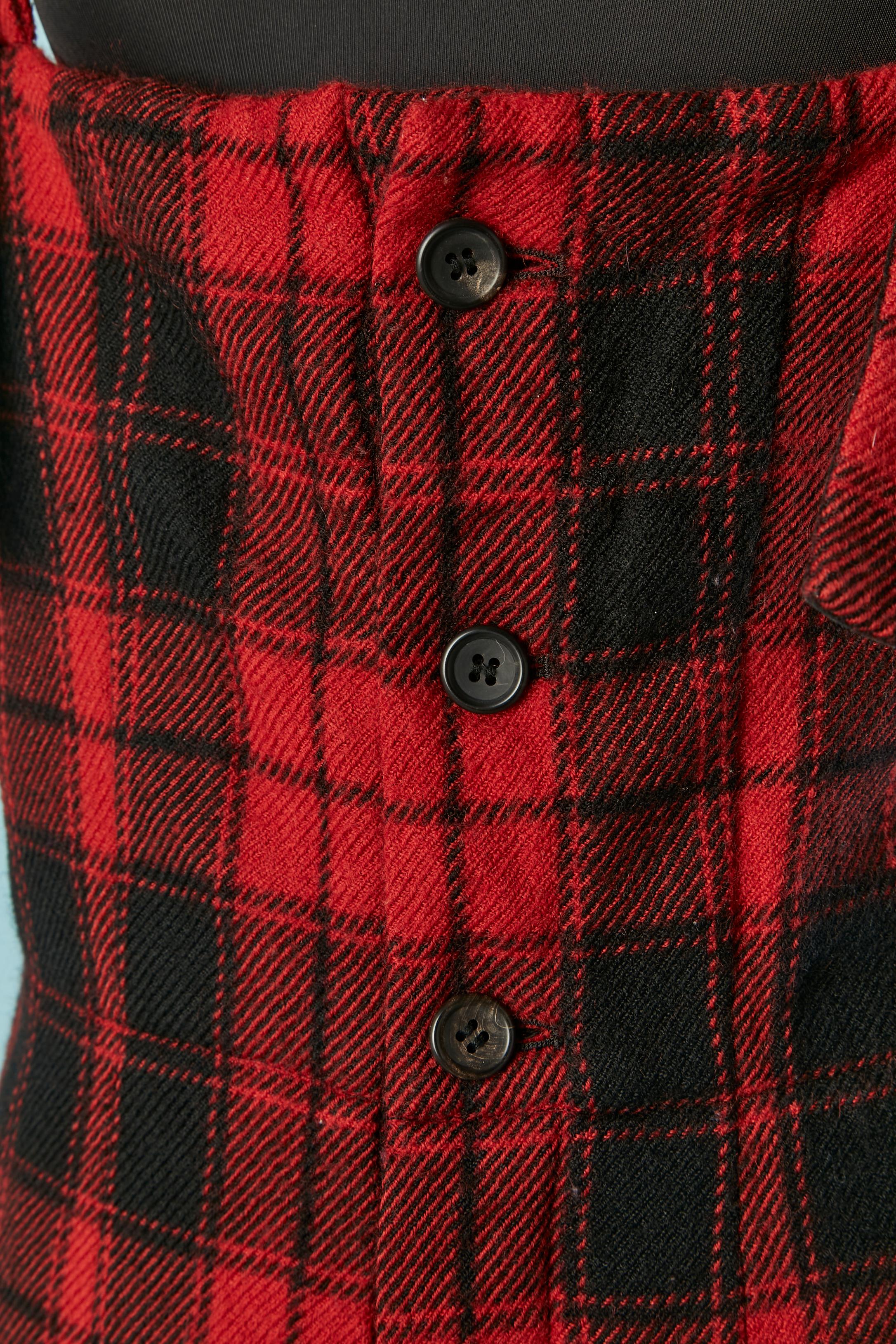 Latzhose aus schwarzer und roter Wolle mit Schottenkaro. Zusammensetzung des Hauptgewebes: 85% Wolle, 15% Nylon. Zusammensetzung des Futters: 100% Cupro. 
Metallschnalle an jedem Schultergurt. 
Knopf und Knopfloch in der vorderen Mitte. 
SIZE 