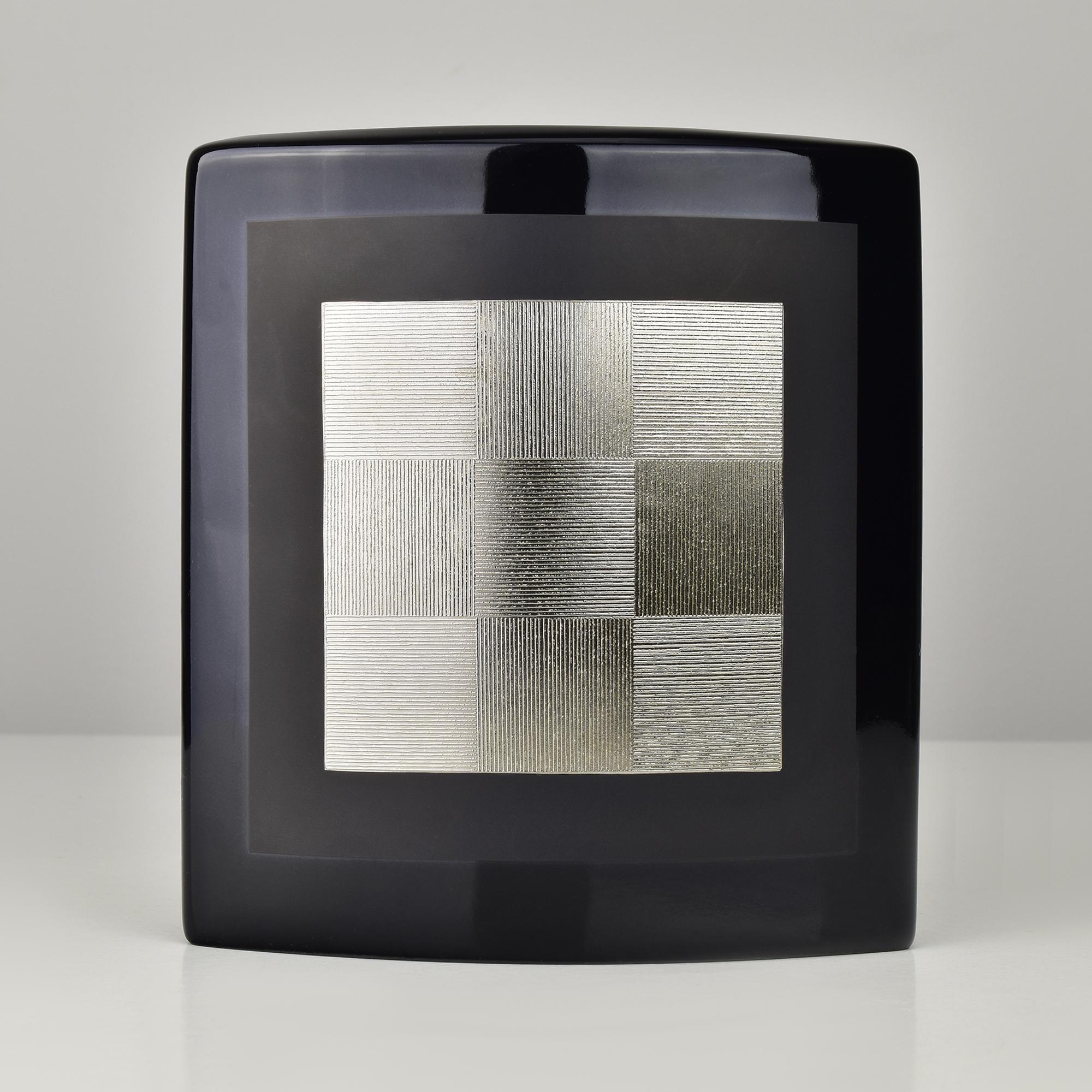 Elegante vaso in porcellana nera disegnato da H. Dressler per Rosenthal, Germania. Il vaso ha una sofisticata forma rettangolare con un corpo leggermente curvo e un motivo a griglia in argento metallico al centro, che crea un raffinato contrasto con