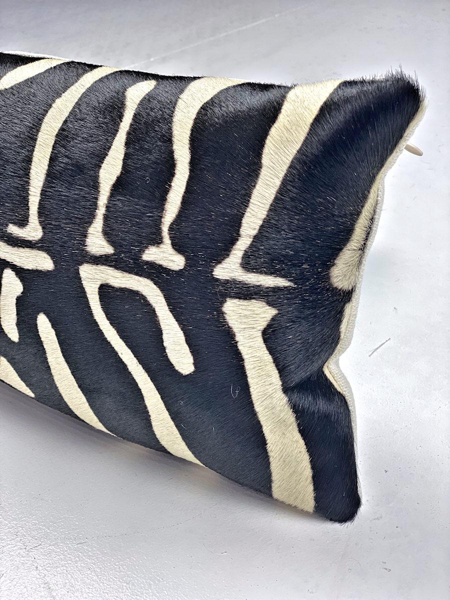 A striking black and white lumbar pillow enhances the contemporary mood of an interior. The slender rectangle pillow is hand-crafted using hair-on cowhide with a screen-printed, tribal abstract design. The black abstract design is printed onto a