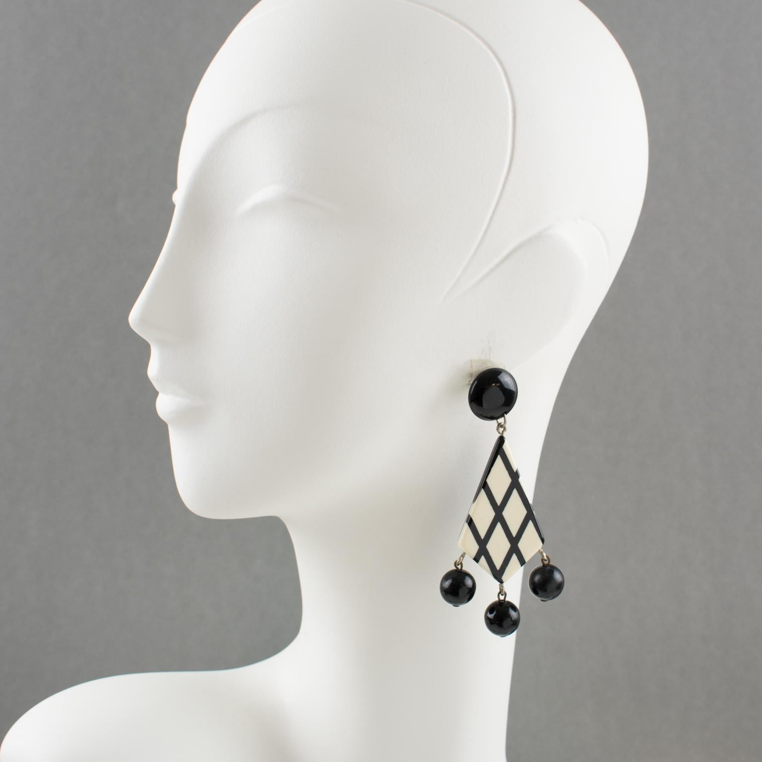 These lovely French Lucite pierced dangling earrings feature a geometric shape with a contrasting black and white checkerboard striped pattern ornate with three black bead charms. The pieces are for pierced ears. There is no visible maker's