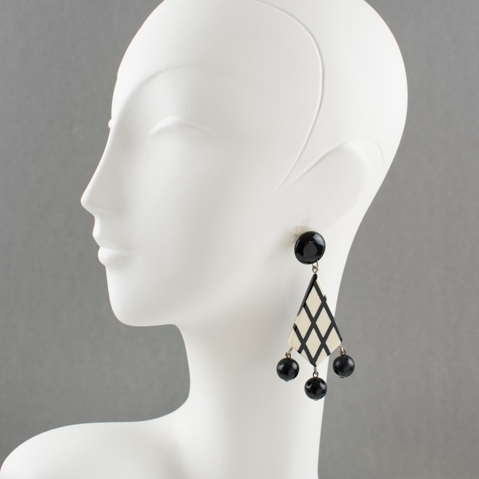 Questi deliziosi orecchini pendenti in lucite francese hanno una forma geometrica con un motivo a strisce a scacchiera bianche e nere a contrasto, ornati da tre charme di perline nere. I pezzi sono per orecchie forate. Non è visibile il marchio del