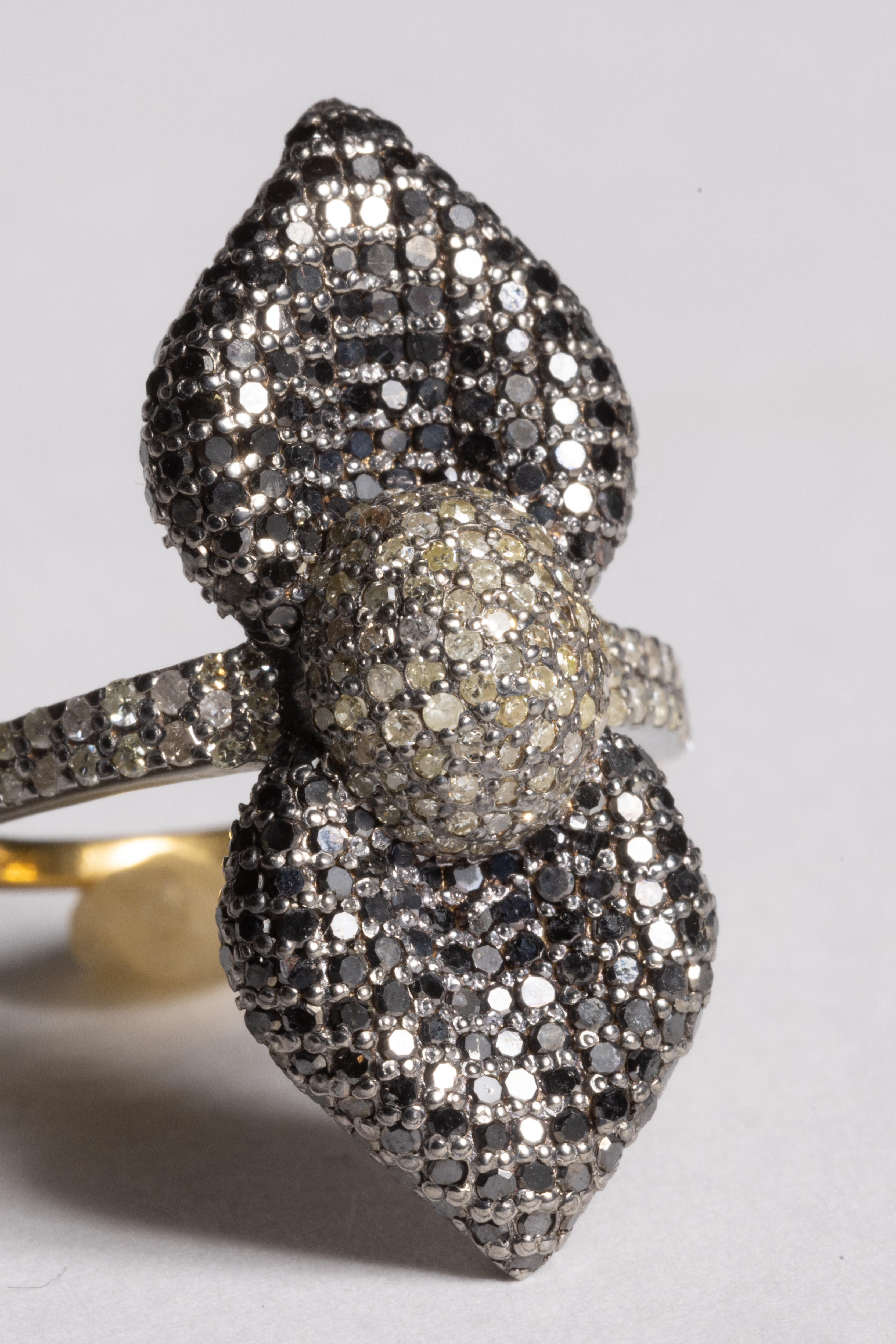 Un extraordinario anillo de cóctel con un motivo floral de doble pétalo, o tal vez un lazo, compuesto por diamantes redondos de talla brillante en el centro y diamantes negros en los pétalos en engaste 