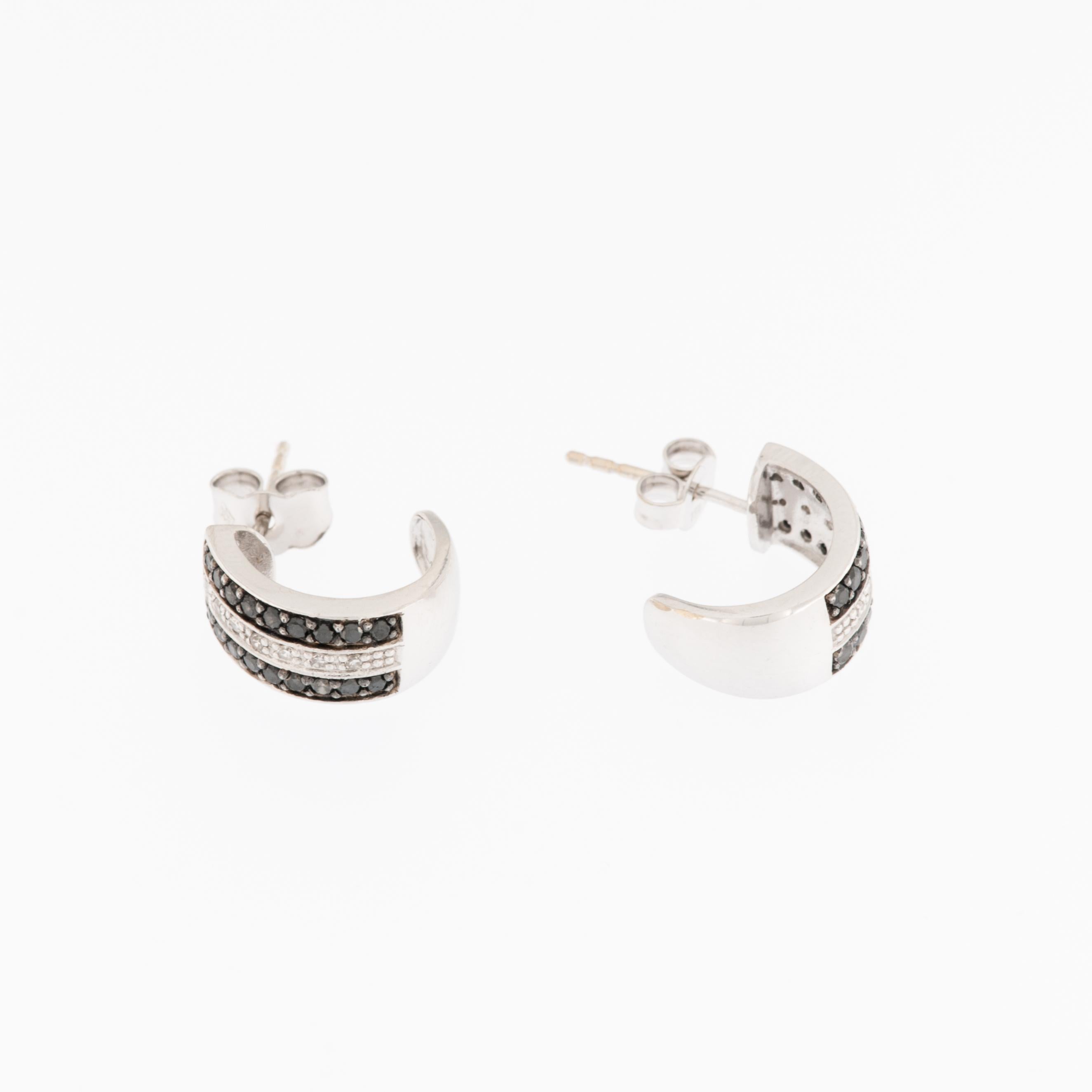 Ces boucles d'oreilles en diamants noirs et blancs, or blanc 18KT, sont un merveilleux bijou conçu pour capter l'attention et l'élégance. 

Les boucles d'oreilles présentent une combinaison de diamants noirs et blancs, taillés en brillant pour un