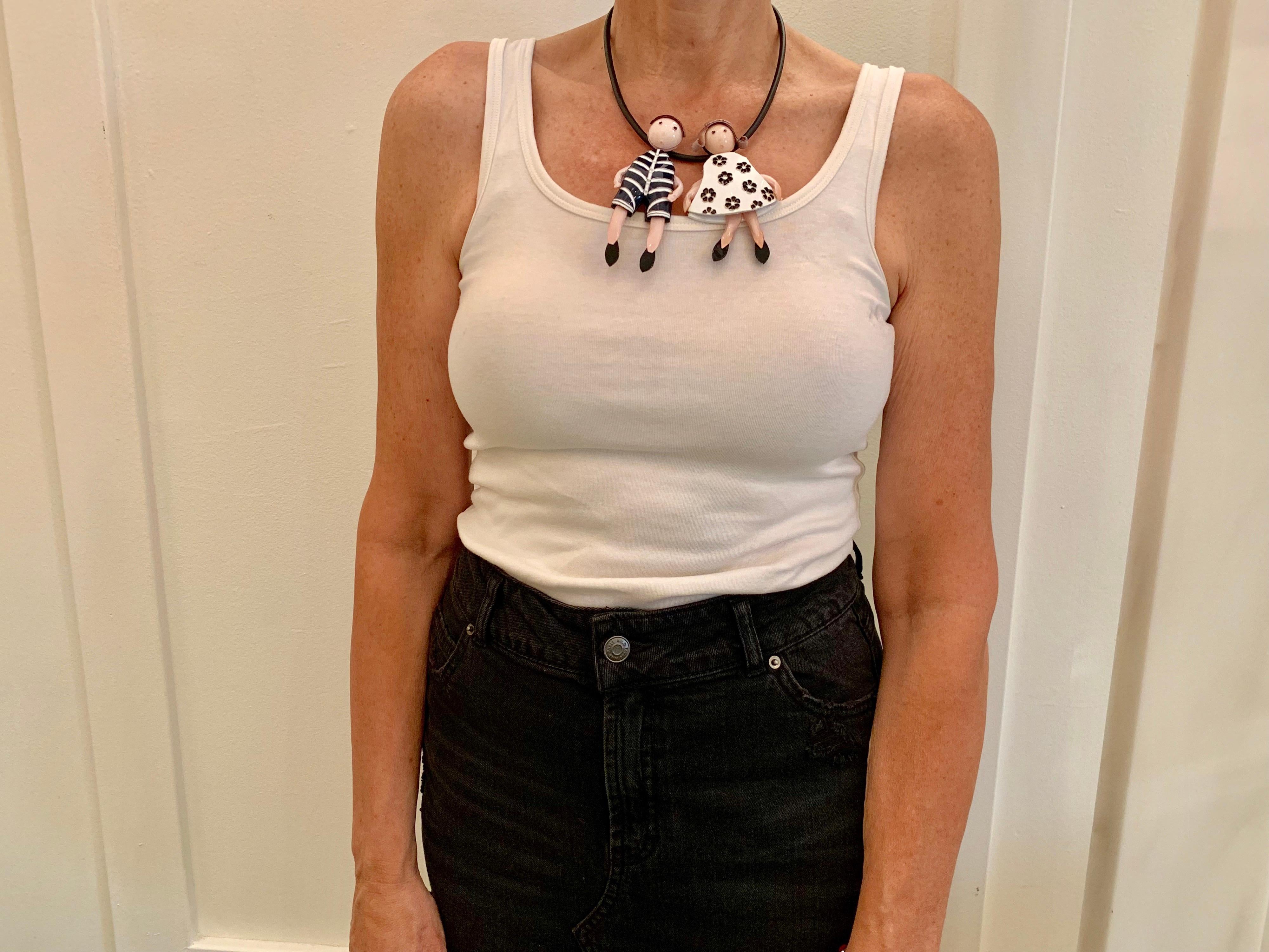 Light and easy to wear, this handmade contemporary artisanal statement pin-necklace was made in Paris by Cilea. The lightweight necklace features two chic Parisian children figures. Both the boy and girls three-dimensional oversized body features
