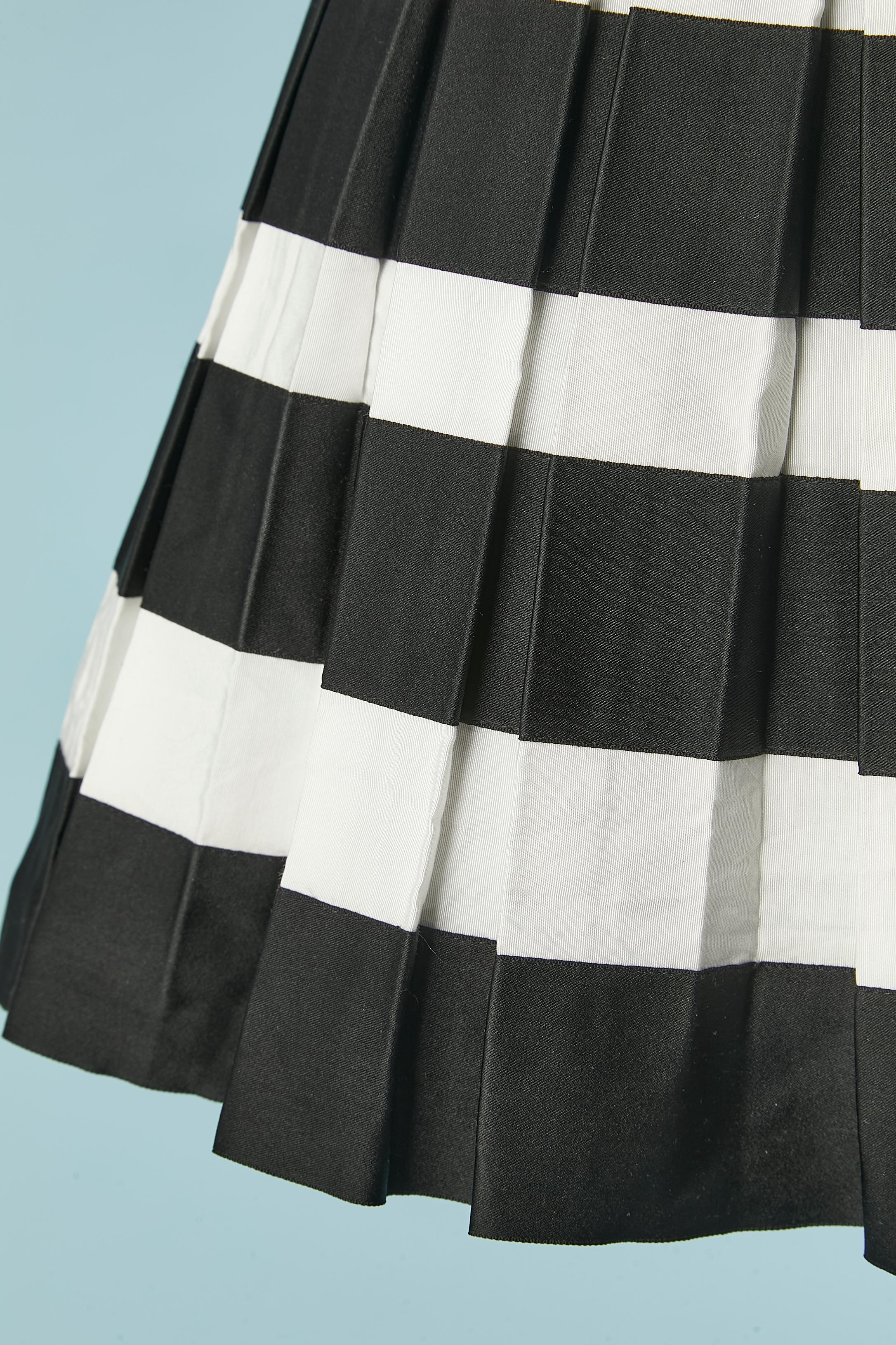 Black and white mini pleated skirt on a top of a A line black silk under-skirt with snap closure. Zip and hook&eye closure in the middle back on the top skirt. Silk top skirt, silk under-skirt and silk branded lining. Small brand brooch on the top