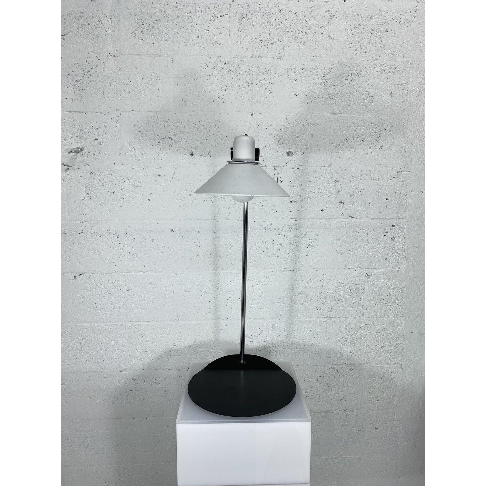 Postmodern lamp with white enameled shade supported by a chrome stem and mounted on a black steel base. The shade tilts back and forth. Not height adjustable.