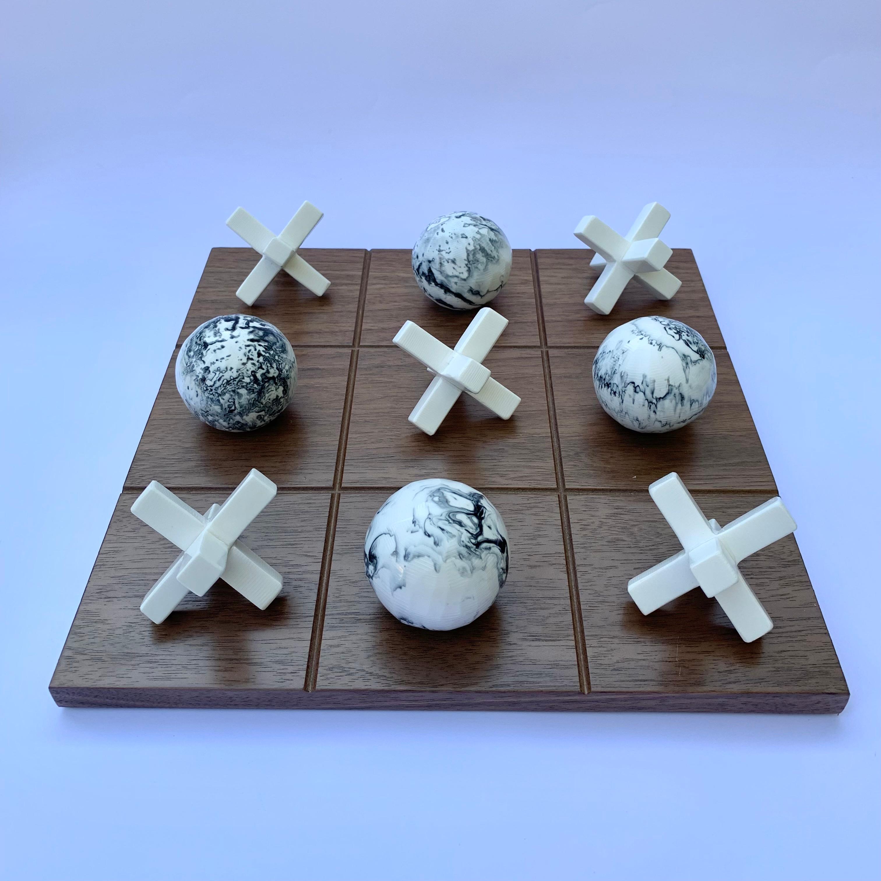 Unser Tic Tac Toe ist eine schöne, moderne und lustige Version des klassischen Spiels. Die dreidimensionalen Stücke sind handgefertigt aus weißem Harz mit schwarzer marmorierter Textur und das Brett ist aus Eichenholzfurnier gefertigt. Es wird das