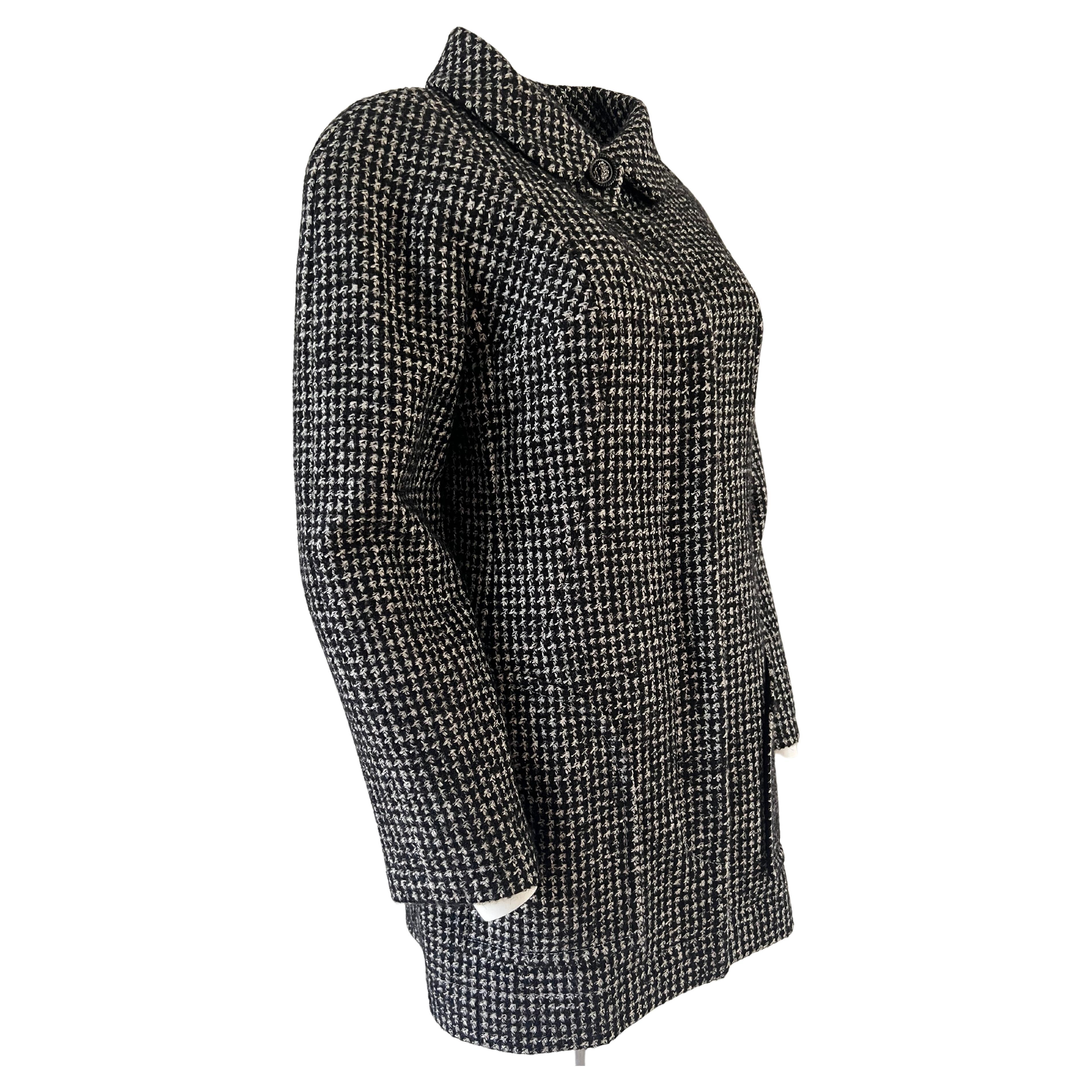 Chanel long jacket in black and white hounds-tooth tweed. Open round neck.
Two large pockets on the front of the jacket with an opening at an angle. Seven buttons in black tones bear the image of a lion's mouth. The buttons are hidden when the