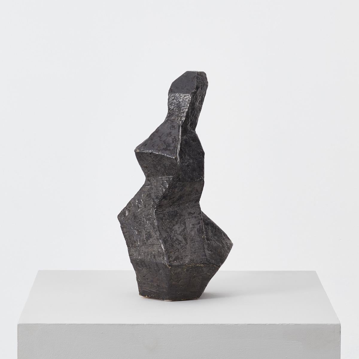 This abstract sculptural work resembles an anthroposophic figure. The disjointed ceramic sculpture has a rough surface and is finished in black glaze, with small peaks of the white underglaze peaking through. Its aesthetic is on point today, fitting