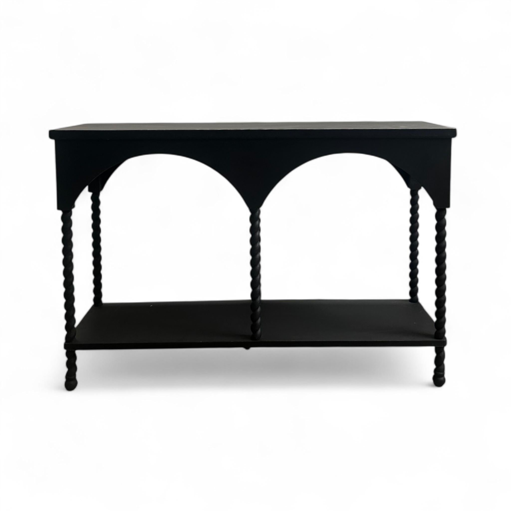 This striking black console features arched detailing and twisted spindle legs for a sculptural, architectural look. A lower shelf offers practical storage or display space, making it as functional as it is eye-catching. Perfect for an entryway,