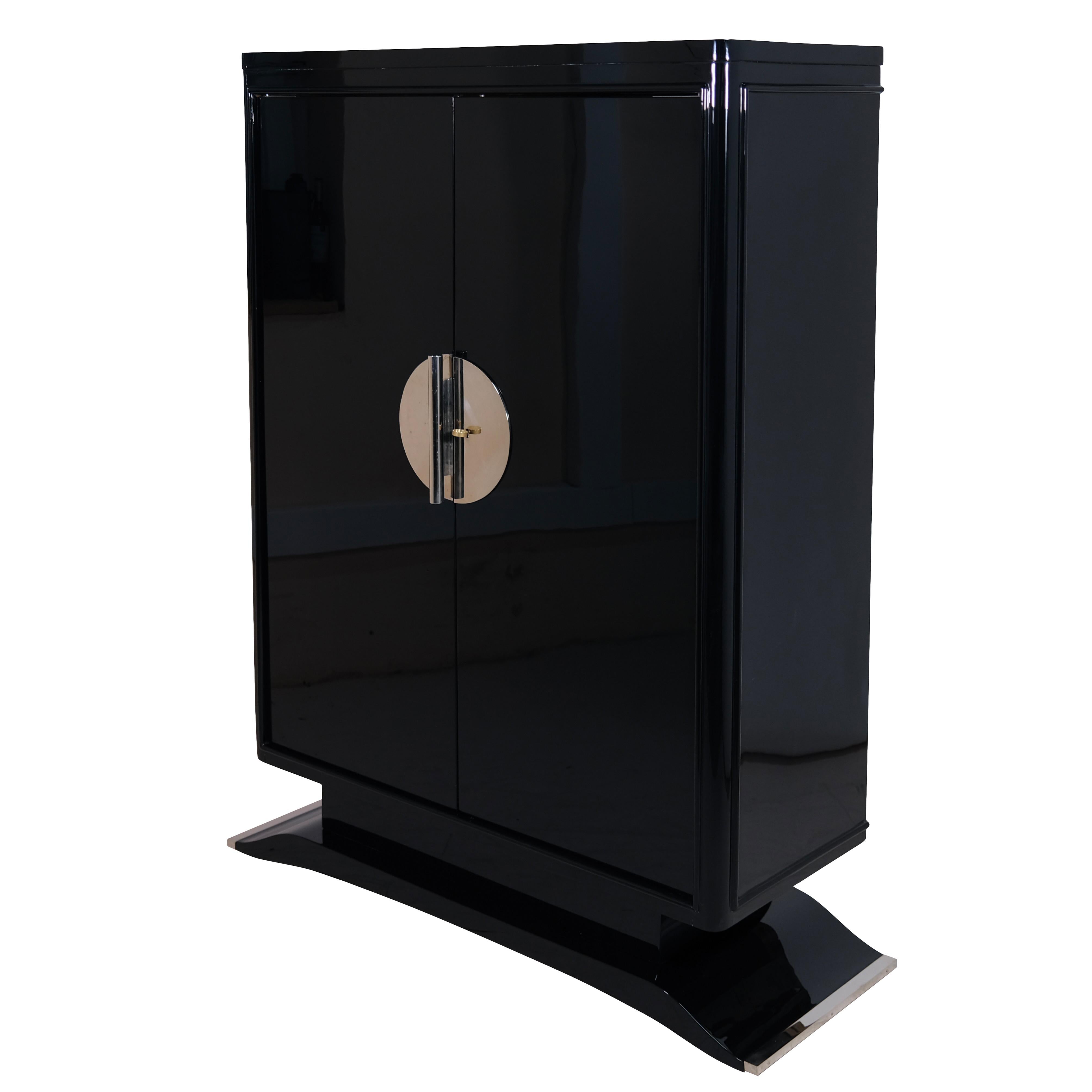 This striking original Art Deco cabinet from 1930s France is a masterclass in sophisticated design and timeless functionality. Finished in a deep, black high-gloss piano lacquer, the piece stands on a subtly curved moustache-shaped base, giving it a