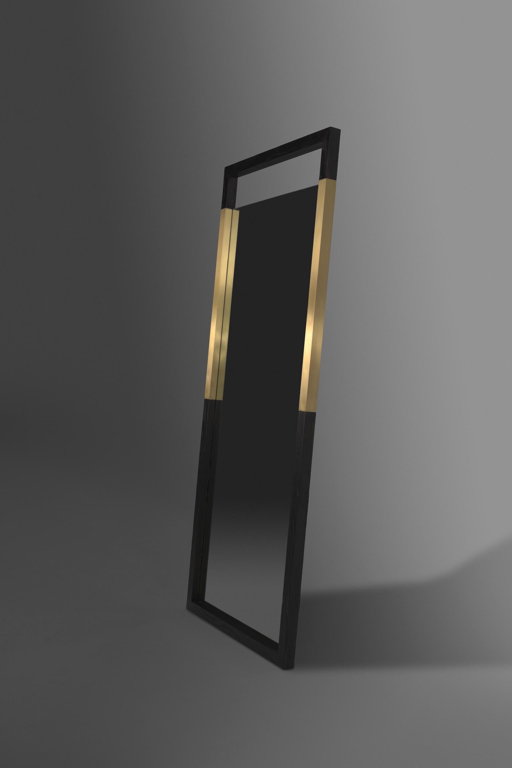 The Broadway standing mirror is a modern mirror made of charred ash wood and brass metal inserts. The open space at the top and bottom add to the modern look of the mirror and allows for the brass to be emphasized even more. This item can also be