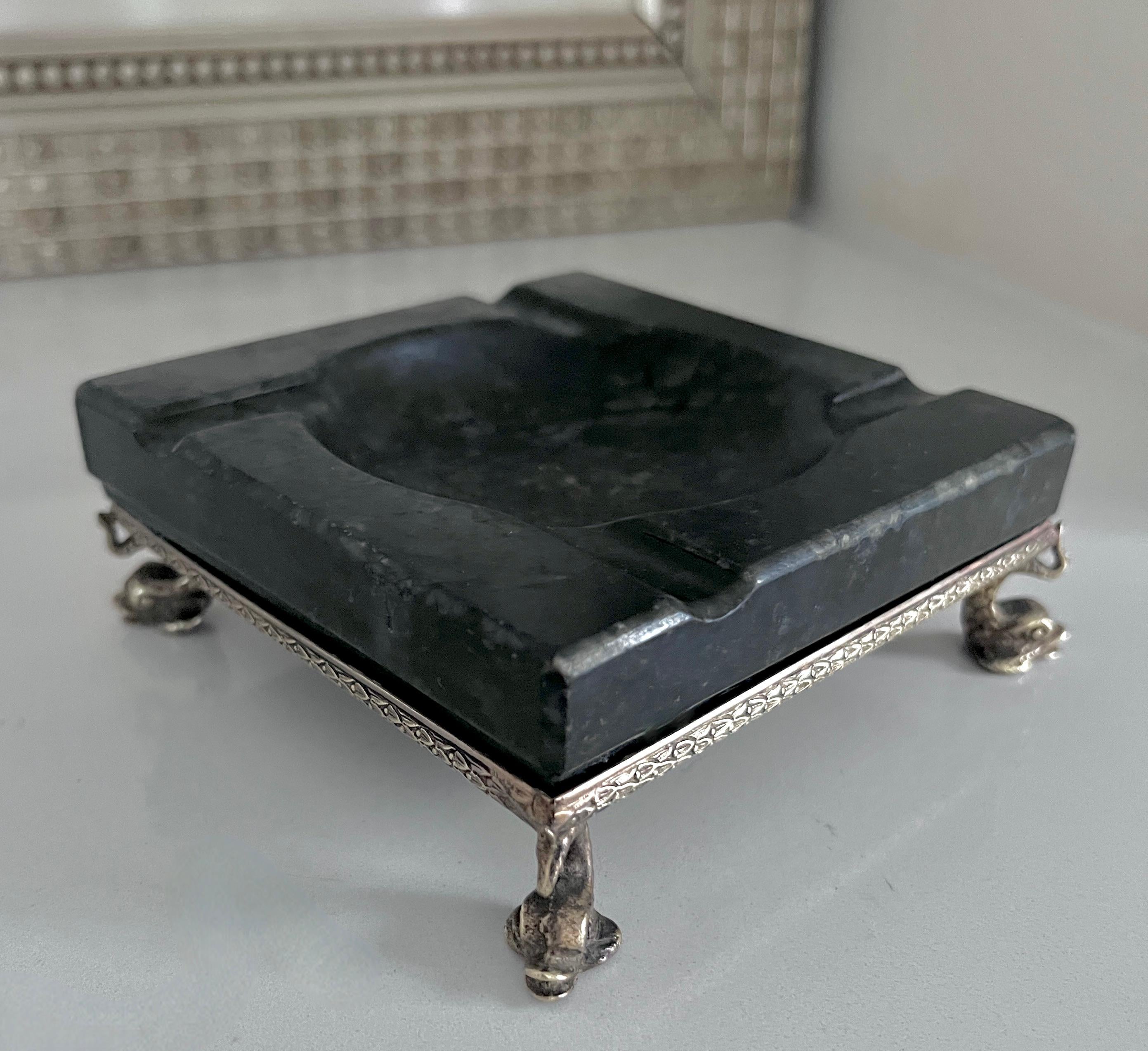 A black stone ashtray sitting in a delicate brass surround held up with legs consisting of Dolphin Serpents.

An elegant piece and a compliment to any bar, cocktail table or outdoor space - a sophisticated and sexy piece, ready for your Cigars,