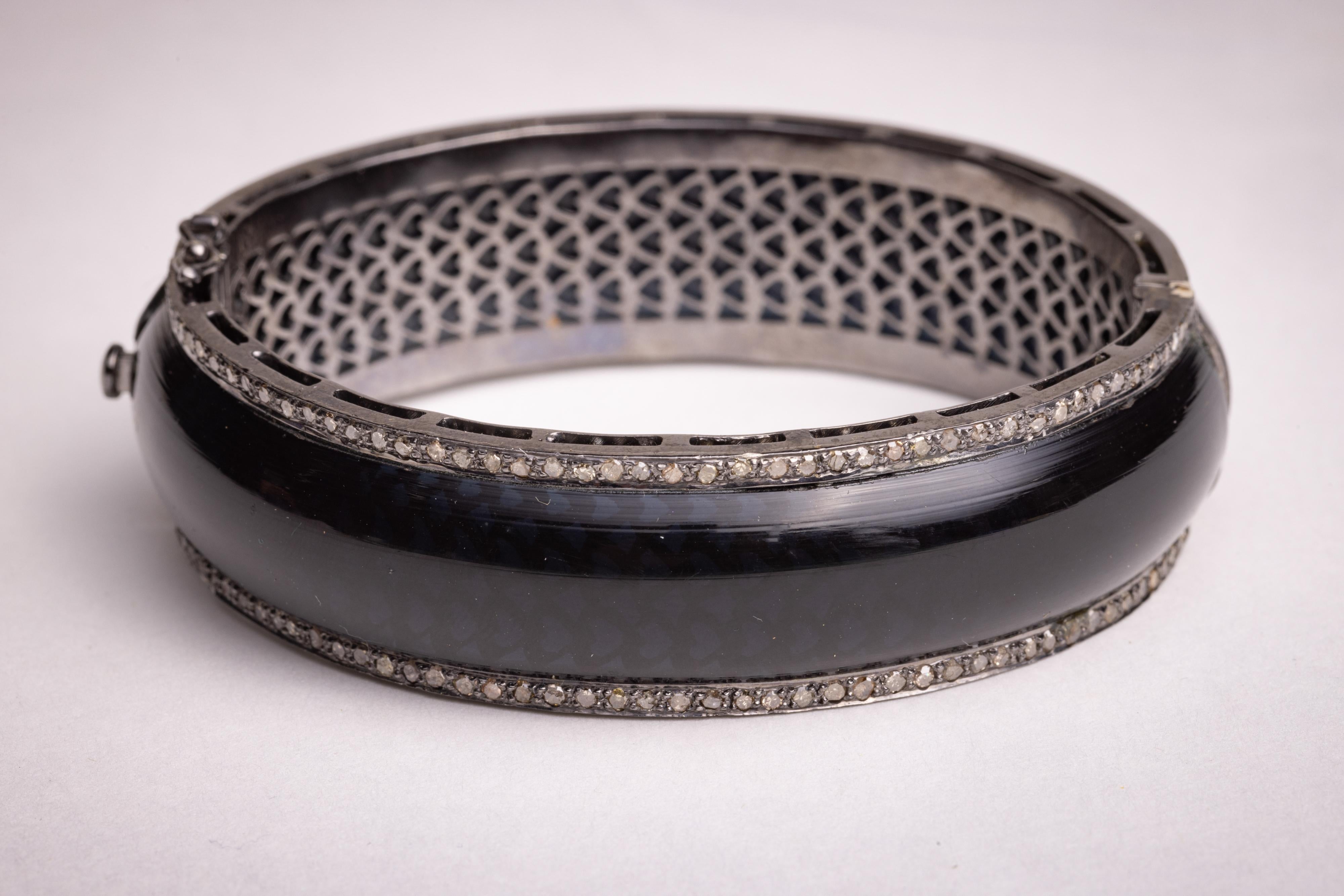 A black Bakelite bangle bracelet bordered on both sides in round, brilliant cut diamonds in a sterling silver pave` setting.  A slight oval shape keeps the bracelet closer to the wrist.  The inside circumference is 6.5